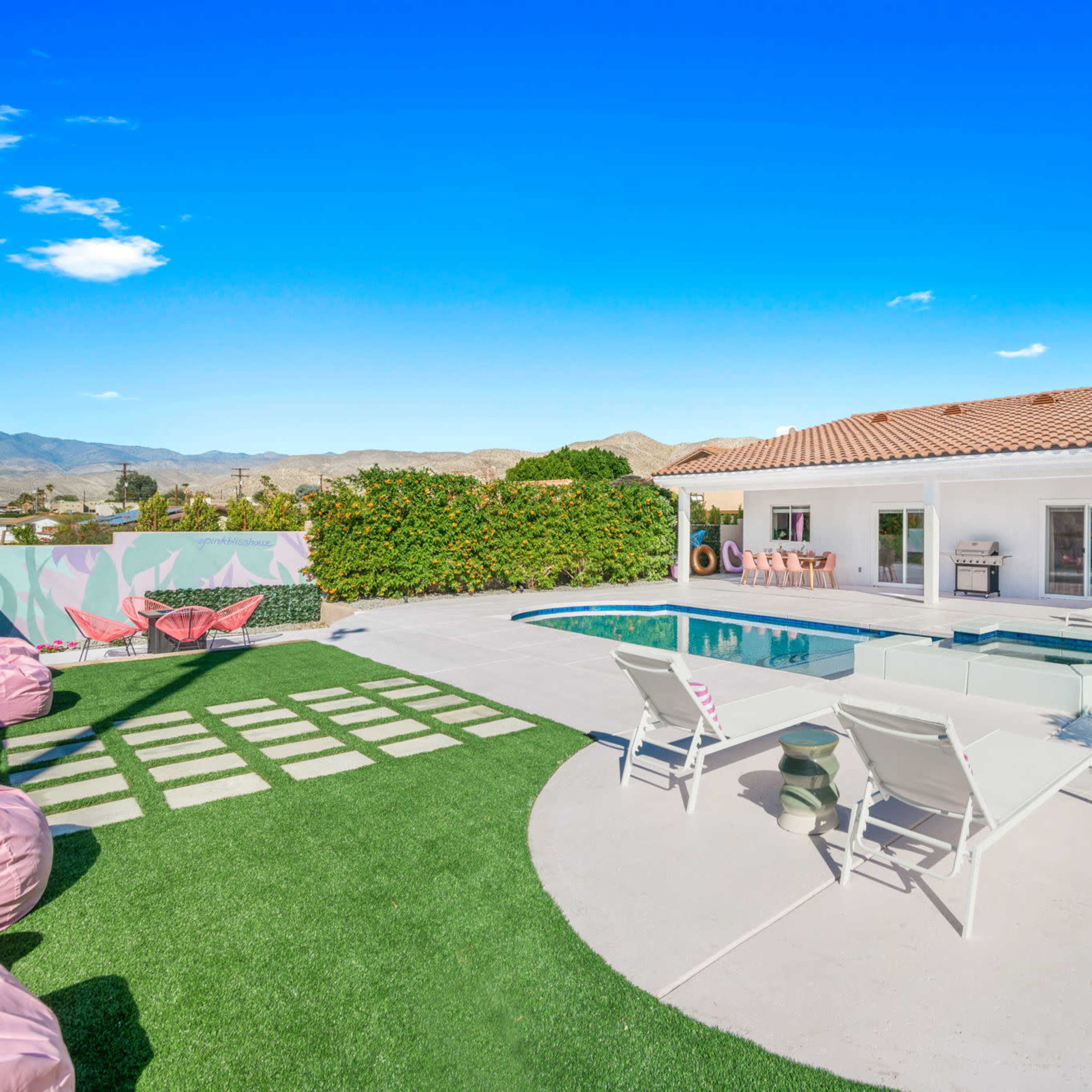 A modern home with a swimming pool and a landscaped yard, featuring lounge chairs and a seating area under a clear blue sky.