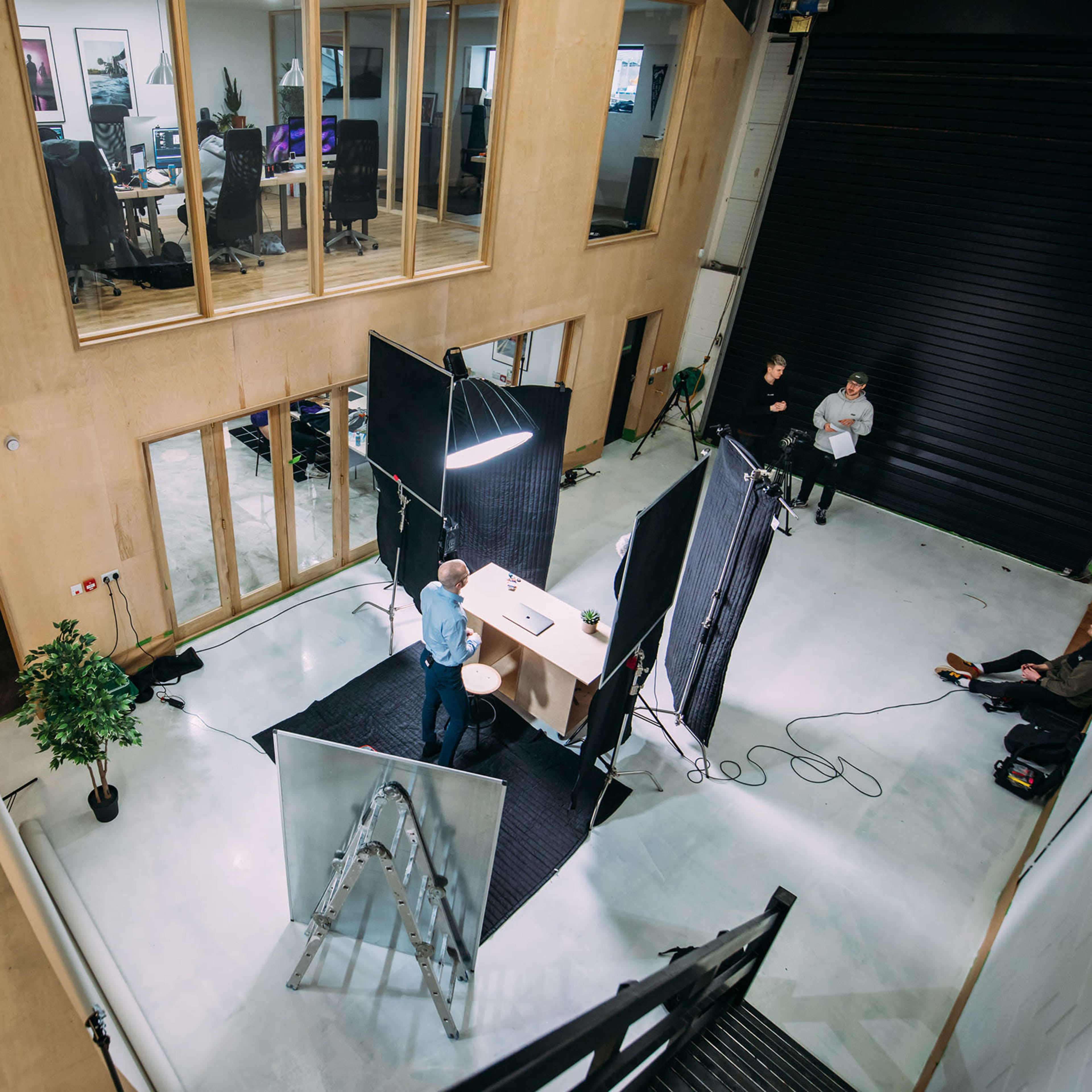 A person stands behind a table with lighting equipment and screens in a spacious, modern office setting.