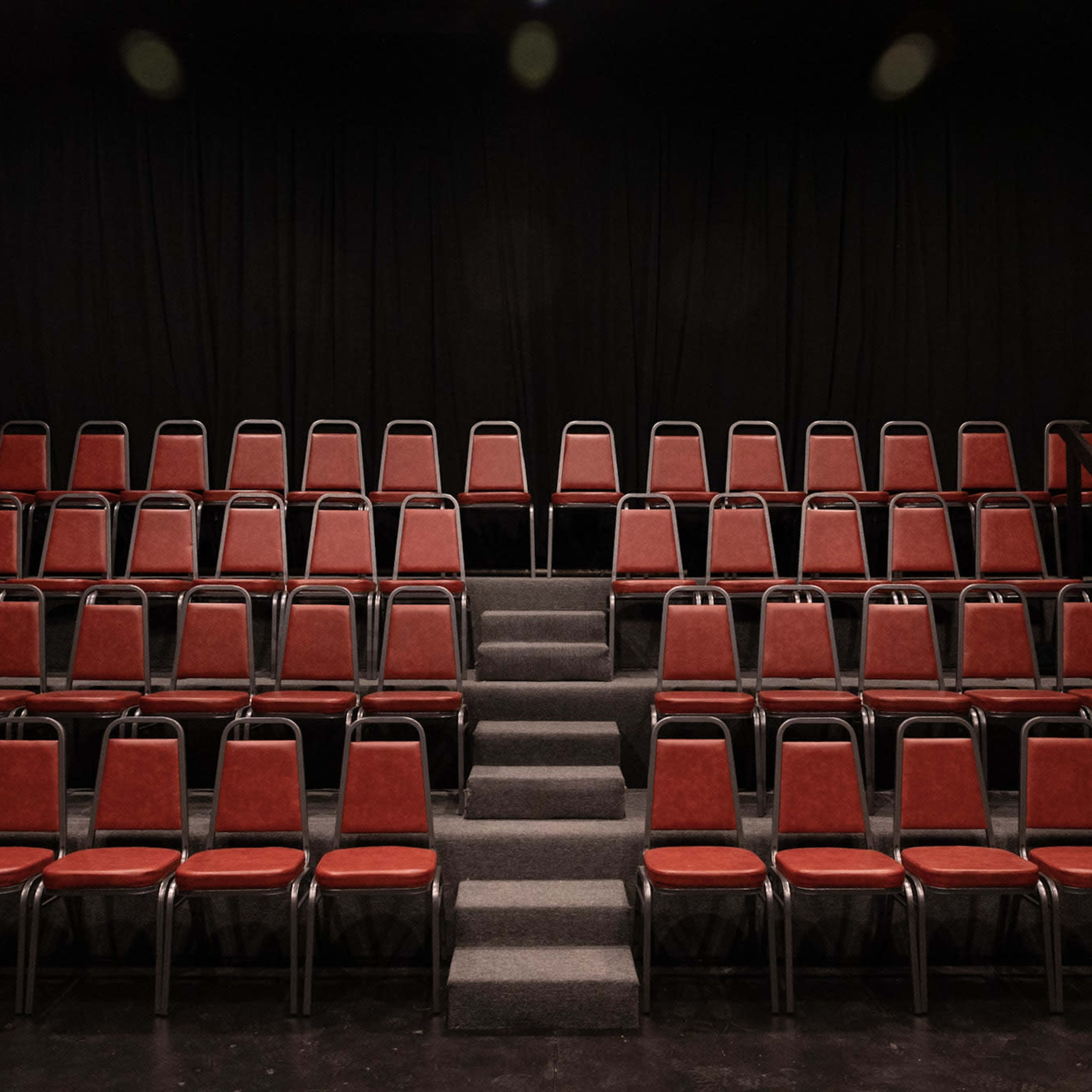 An empty theater seating area with red chairs arranged in rows and a central staircase leading to the upper level.