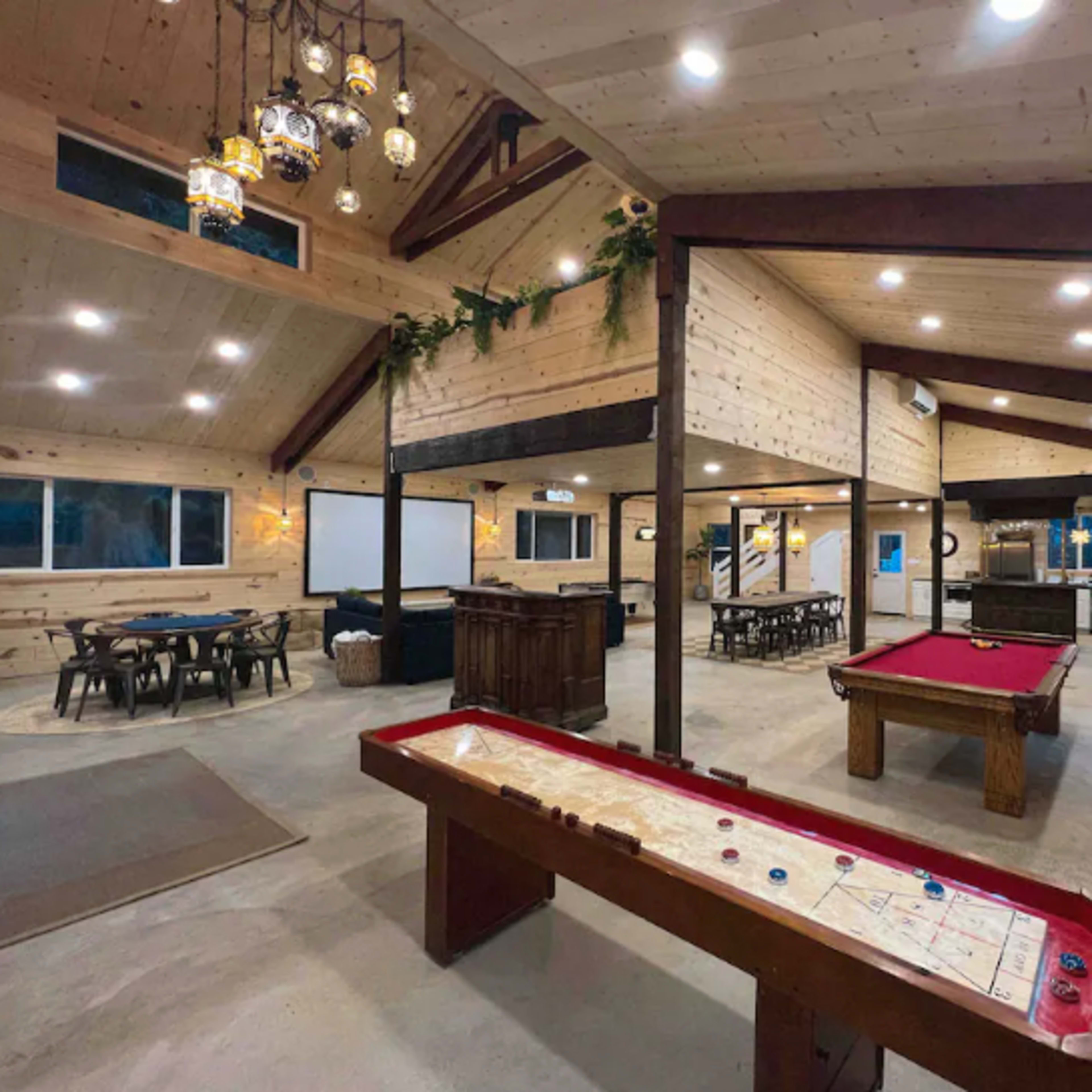 A spacious, wooden interior featuring various game areas, including a pool table, air hockey table, and multiple seating arrangements.