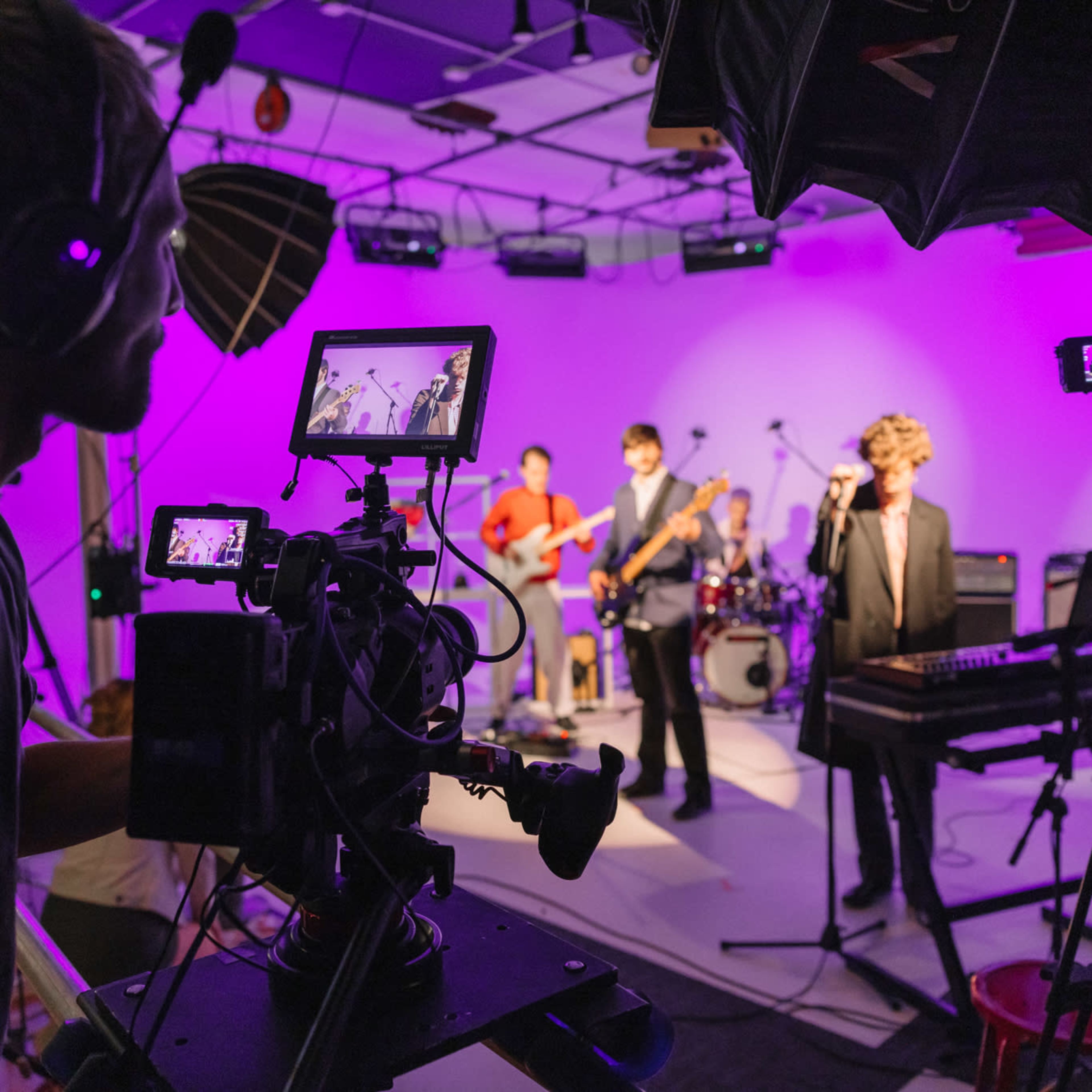 A band performs on stage while a camera operator records the performance on a video camera.