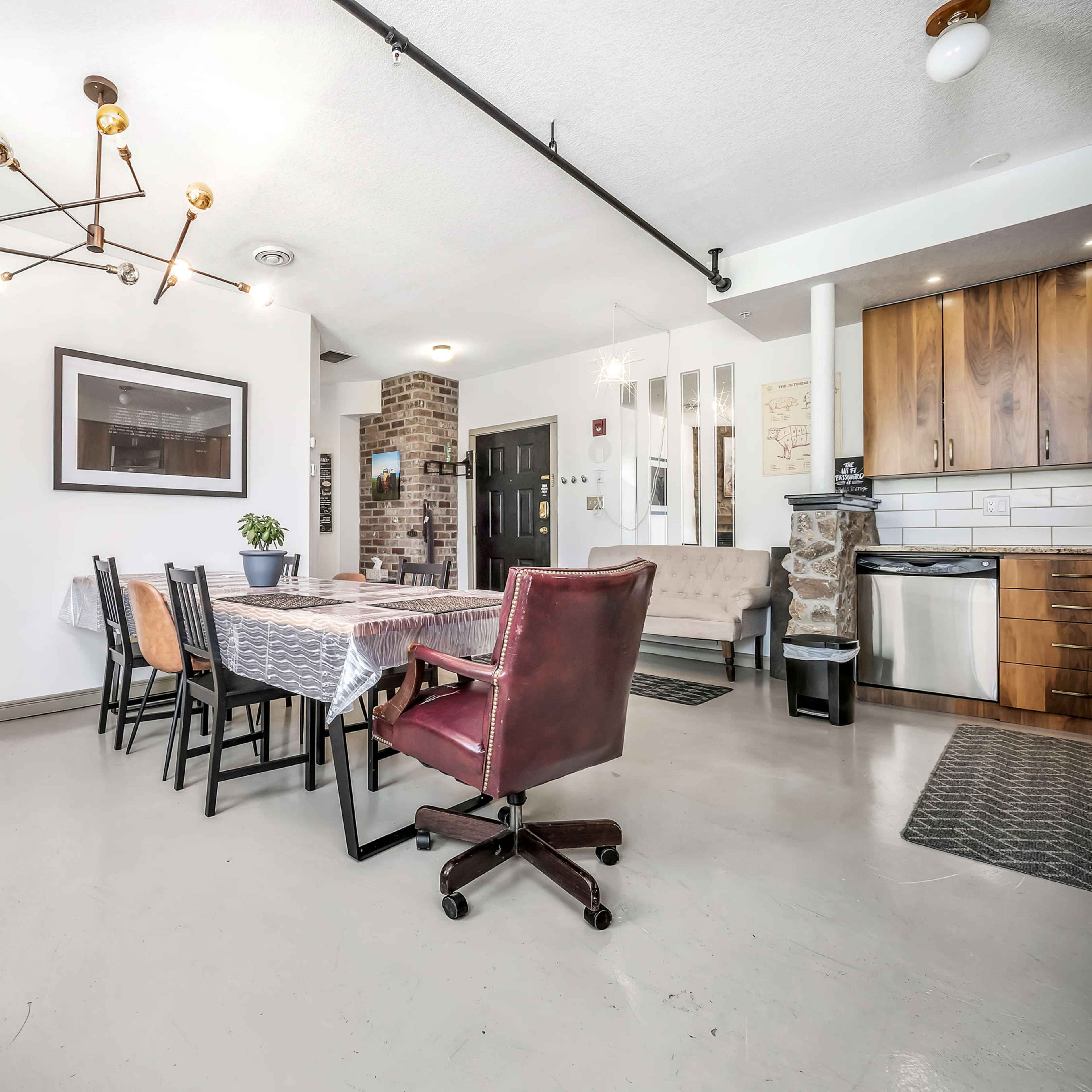 A modern, open-concept living space featuring a stone fireplace, a dining table set for several people, and a kitchen area with wooden cabinets.