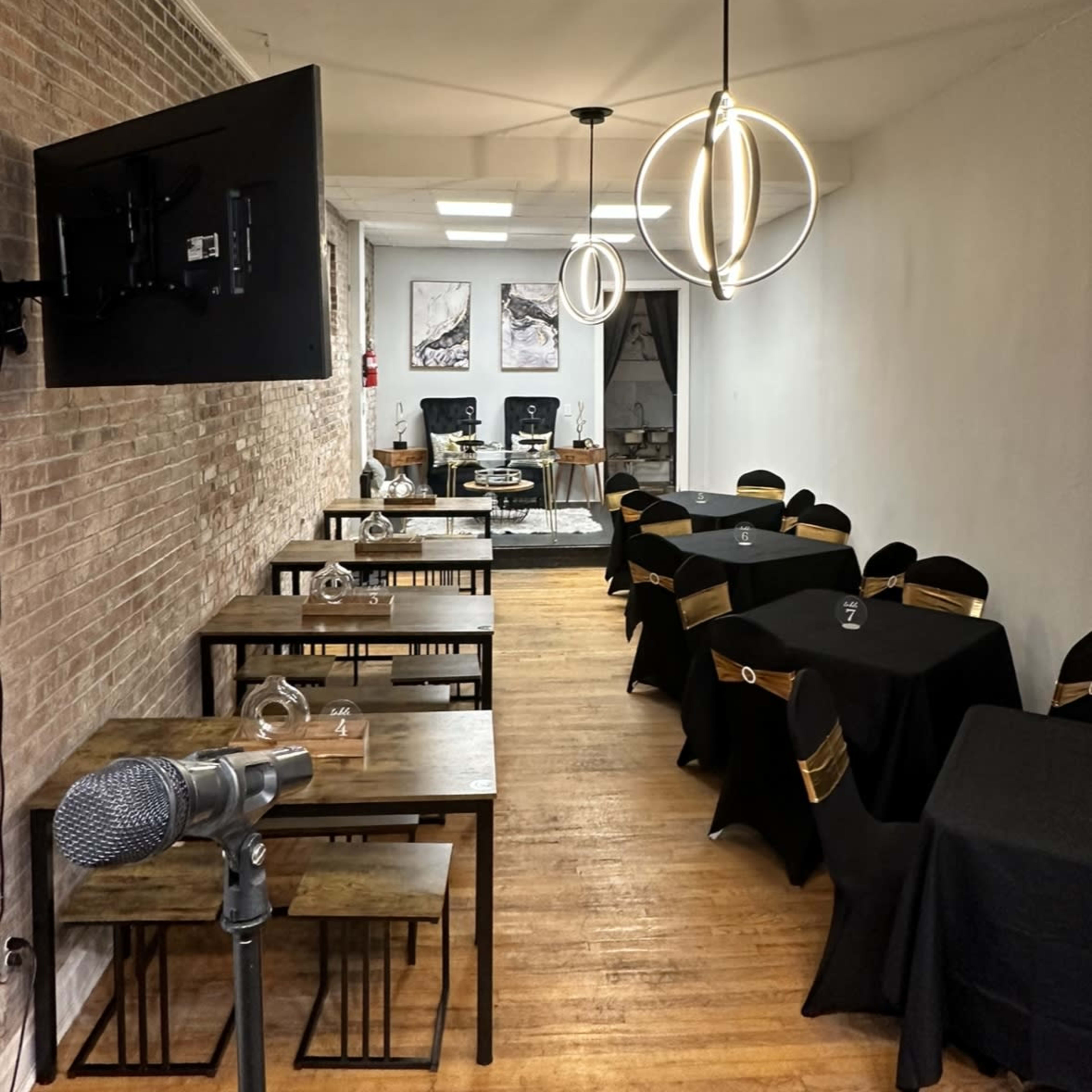 A narrow restaurant with dark tables and chairs, illuminated by modern pendant lights, and featuring a microphone in the foreground.