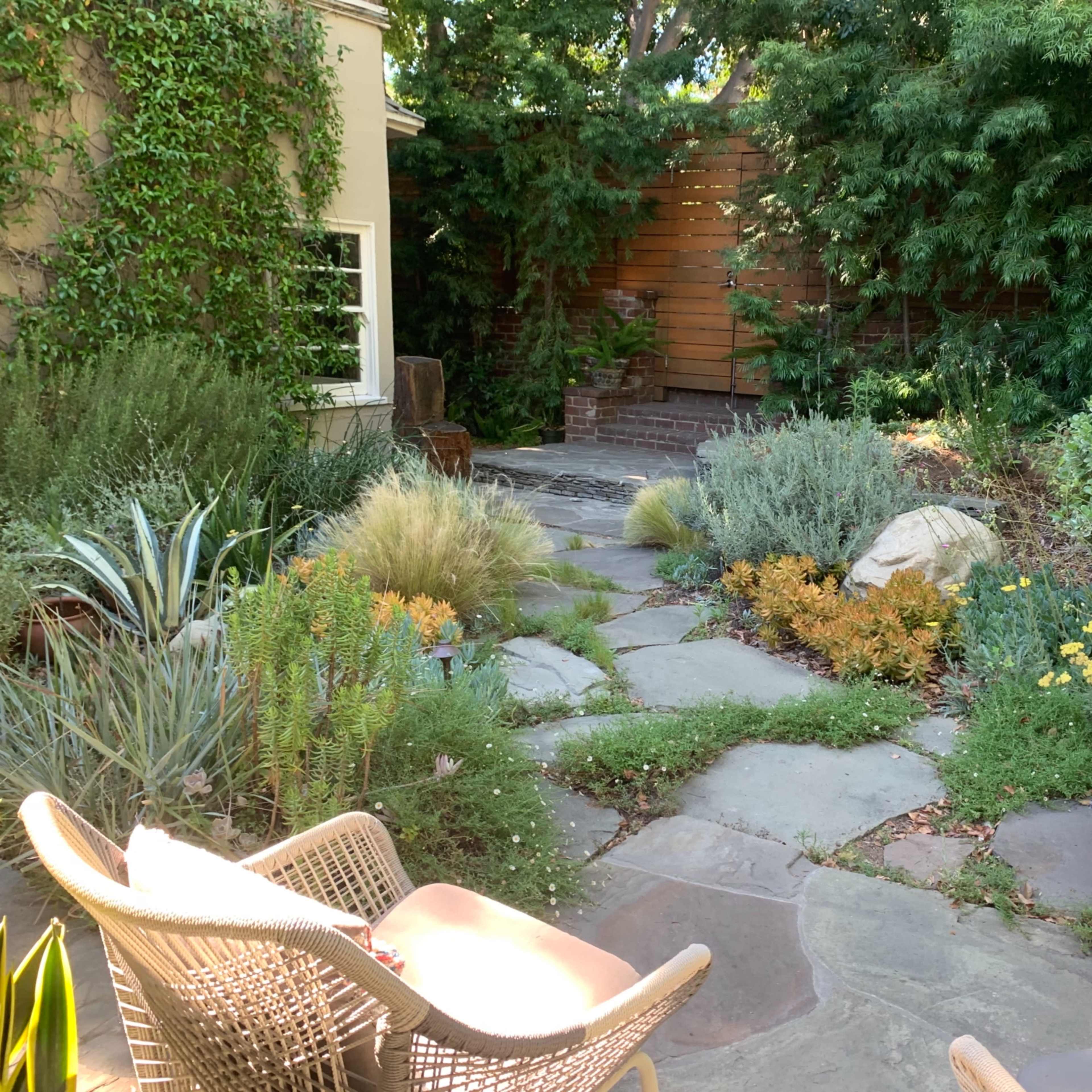 A landscaped garden with stone pathways, various plants, and seating arranged in a serene outdoor setting.