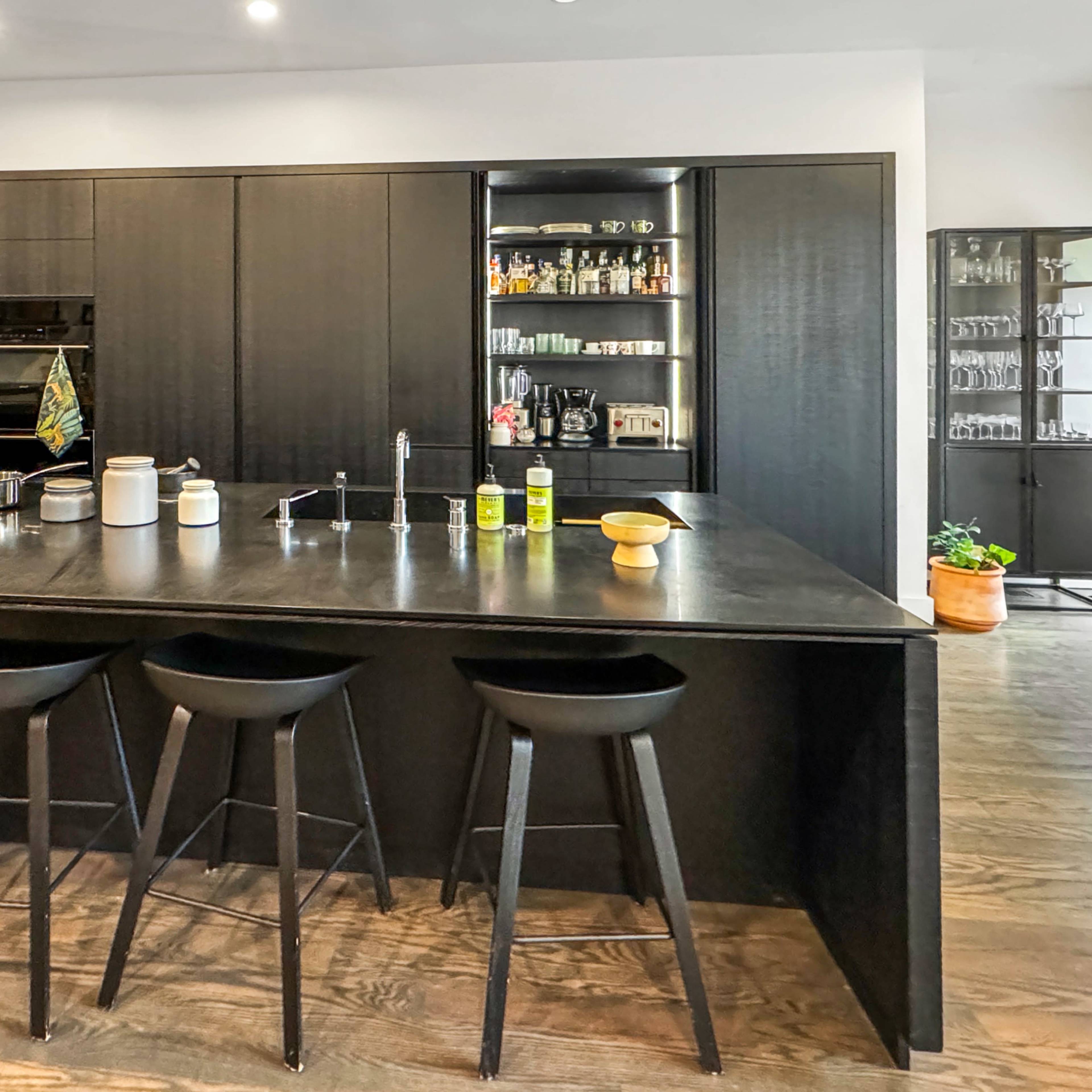 A modern kitchen with a large black island, sleek cabinetry, and high stools arranged around the island.