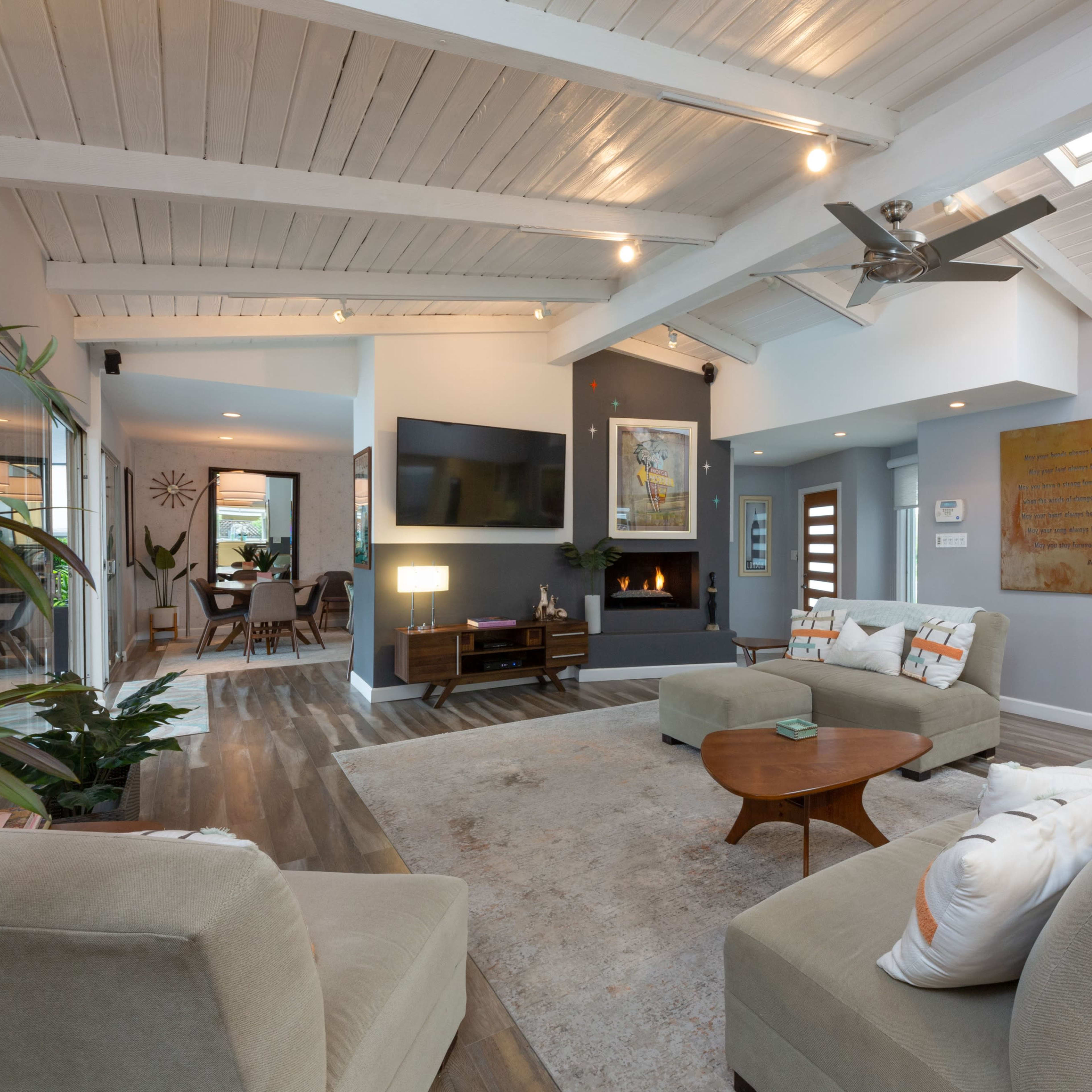 A modern living room with a high ceiling, featuring a seating area, a fireplace, a large flat-screen TV, and decorative artwork on the walls.