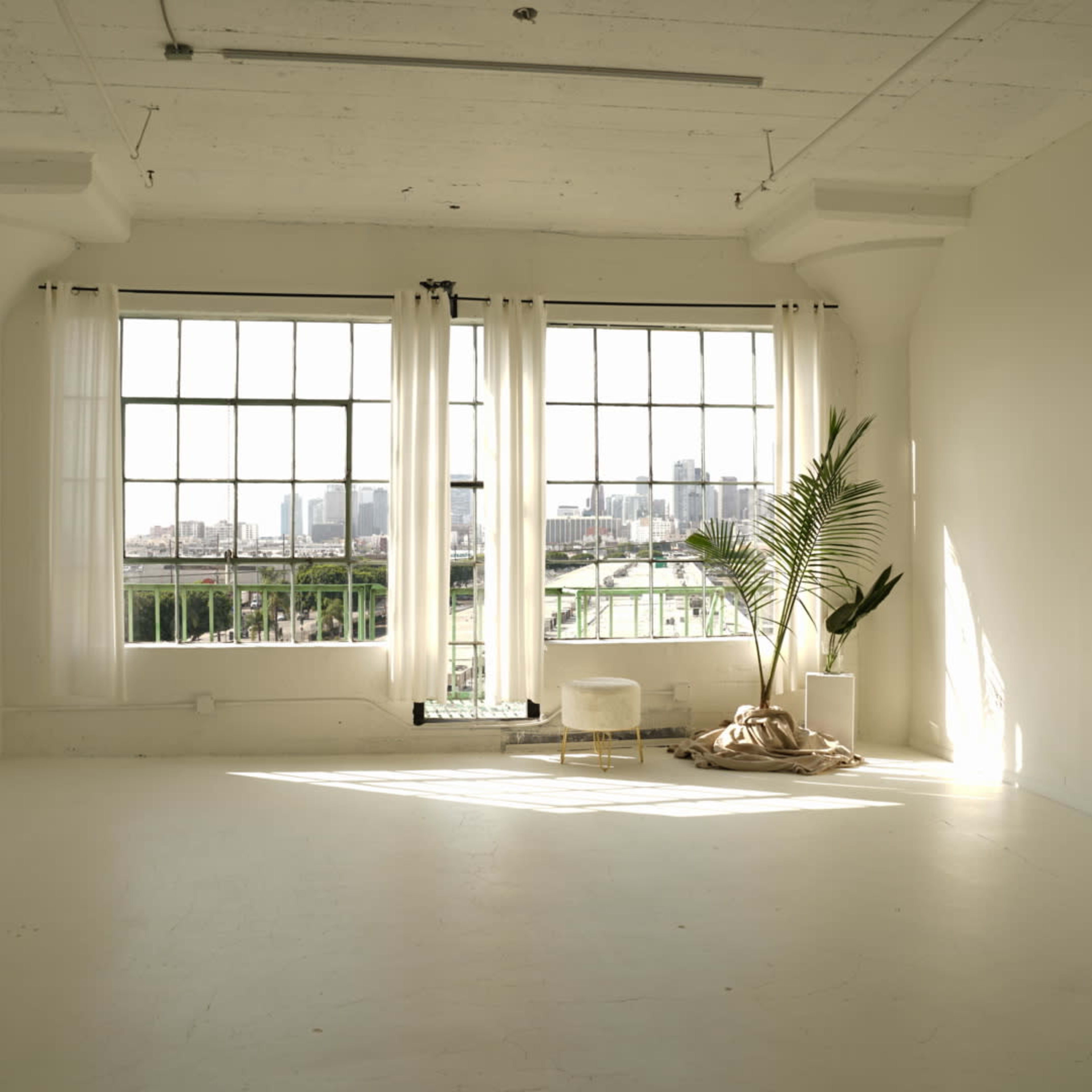 A bright, minimalist room with large windows, sheer curtains, a potted plant, and a small chair.