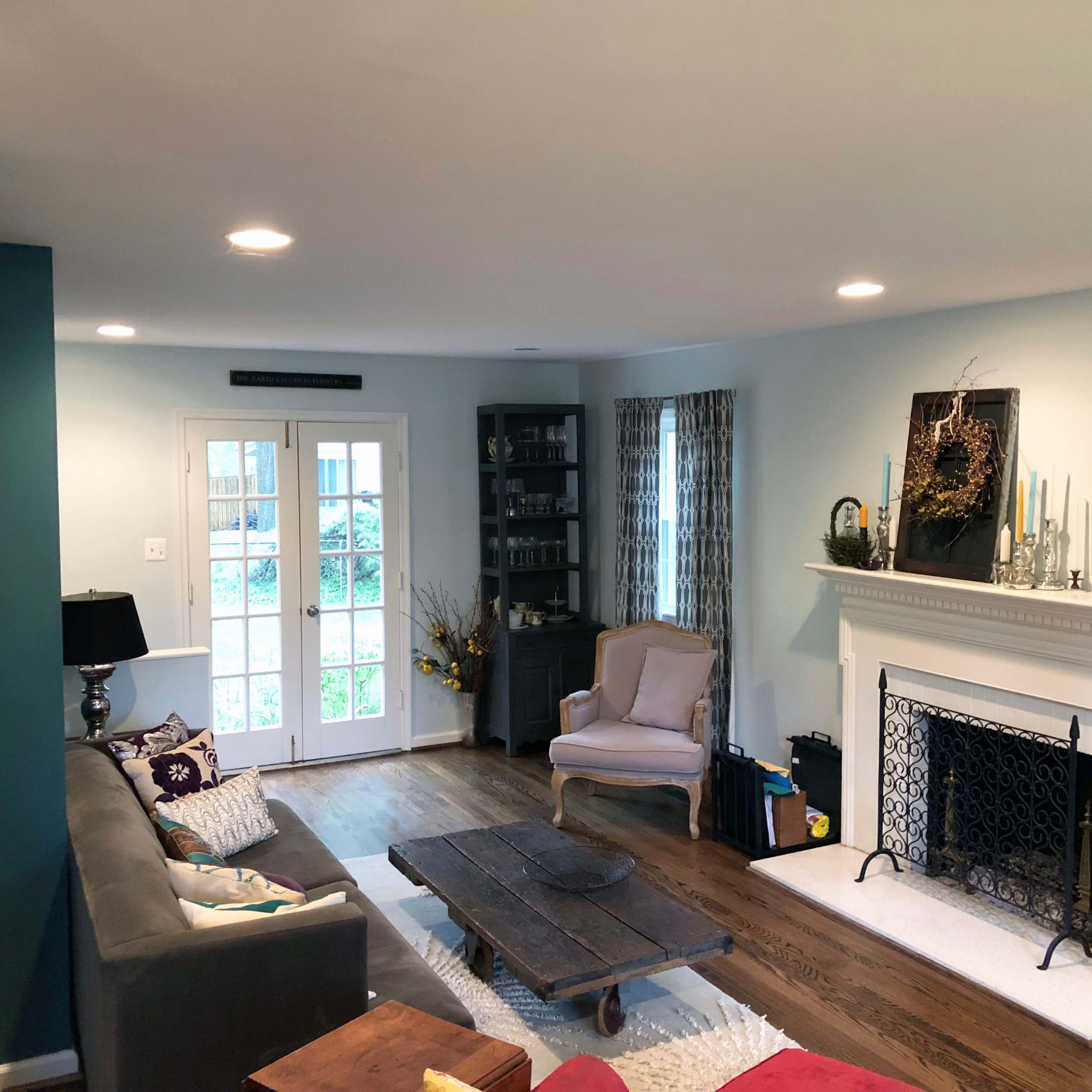 A living room with a sofa, coffee table, armchair, fireplace, and large windows leading to an outdoor area.