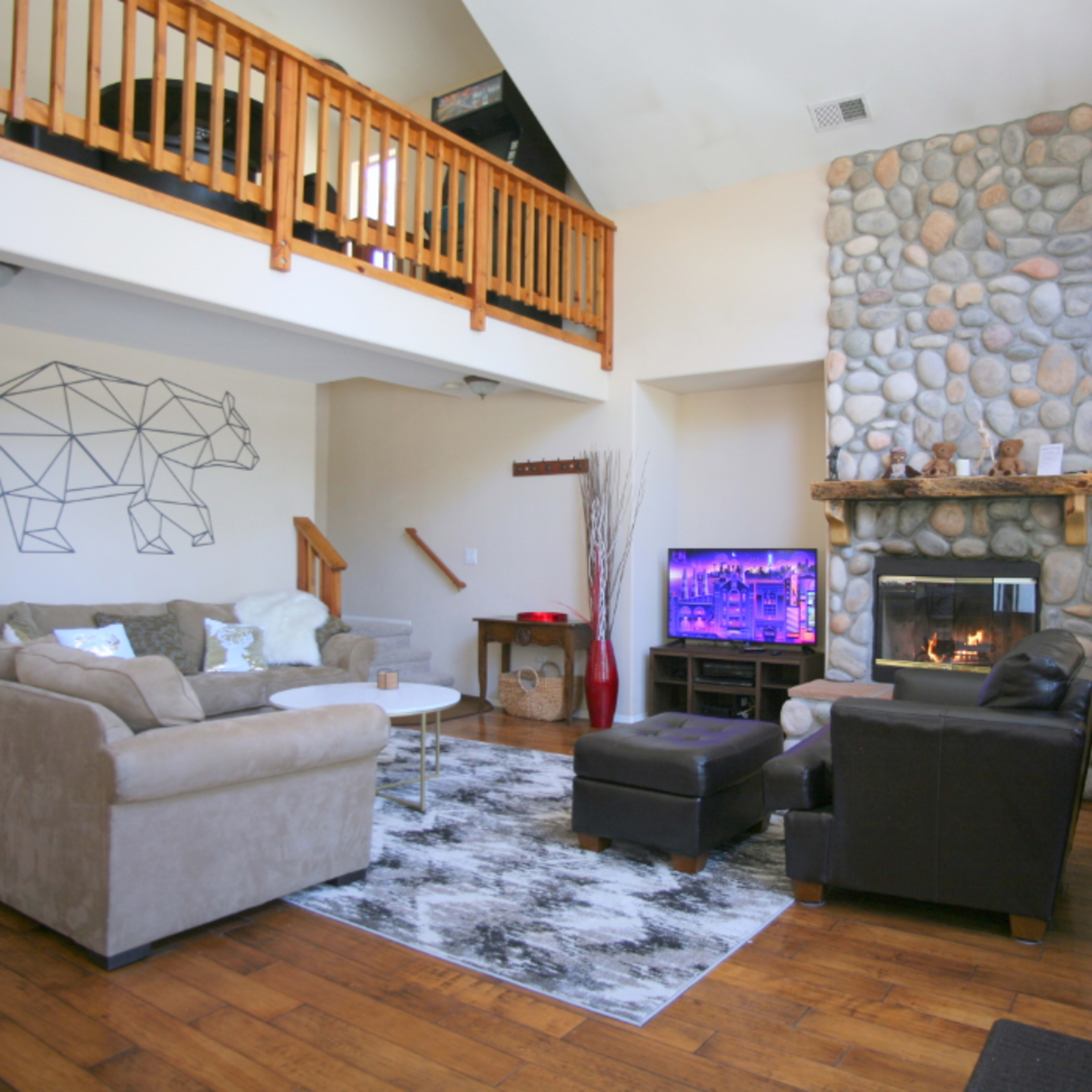The living room features a stone fireplace, a mounted TV, a geometric bear design on the wall, and a mix of seating arrangements including sofas and a coffee table.