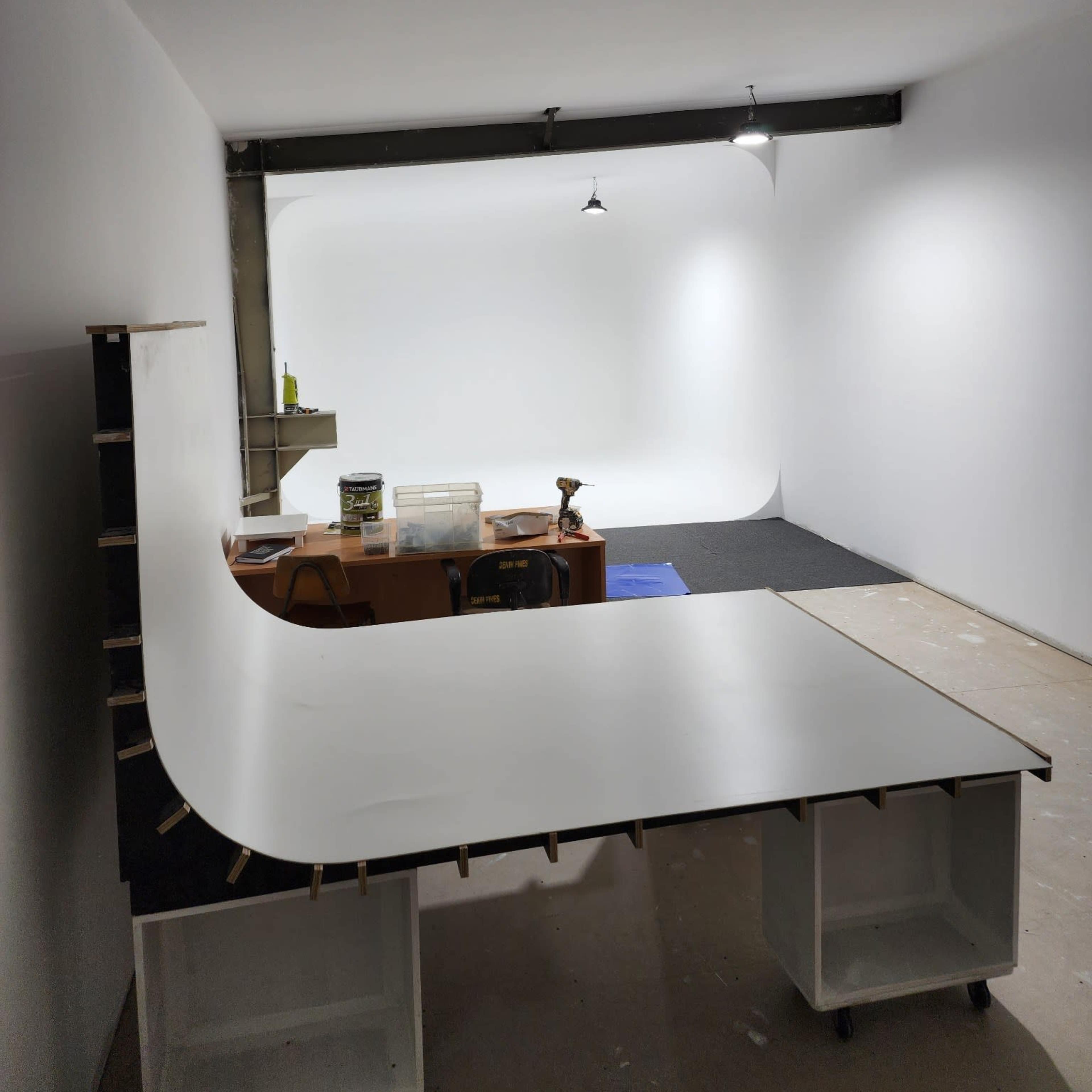 A minimalist interior of a photo studio featuring a white backdrop, a work table, and some tools.