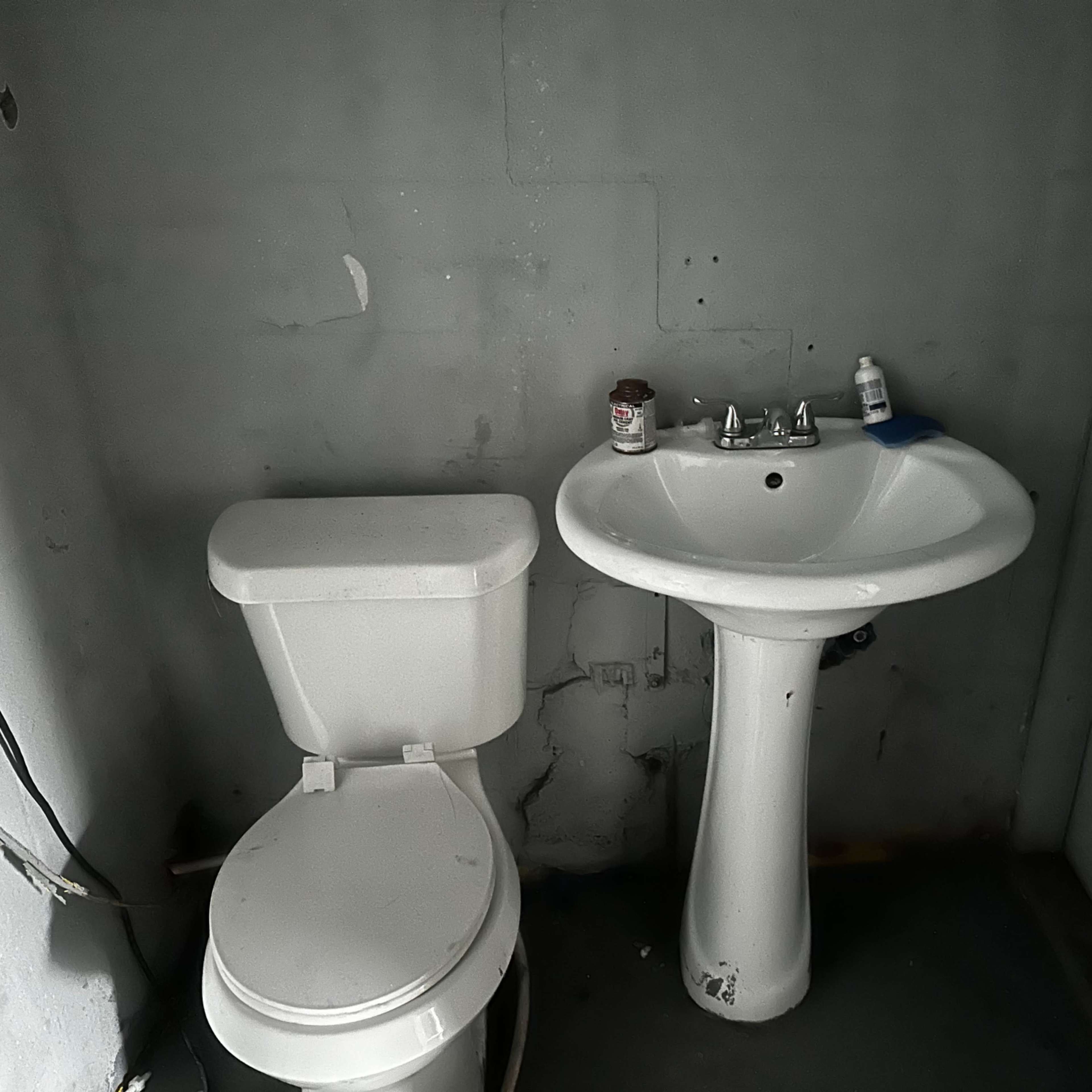 A simple bathroom with a toilet and a sink against a bare gray wall.