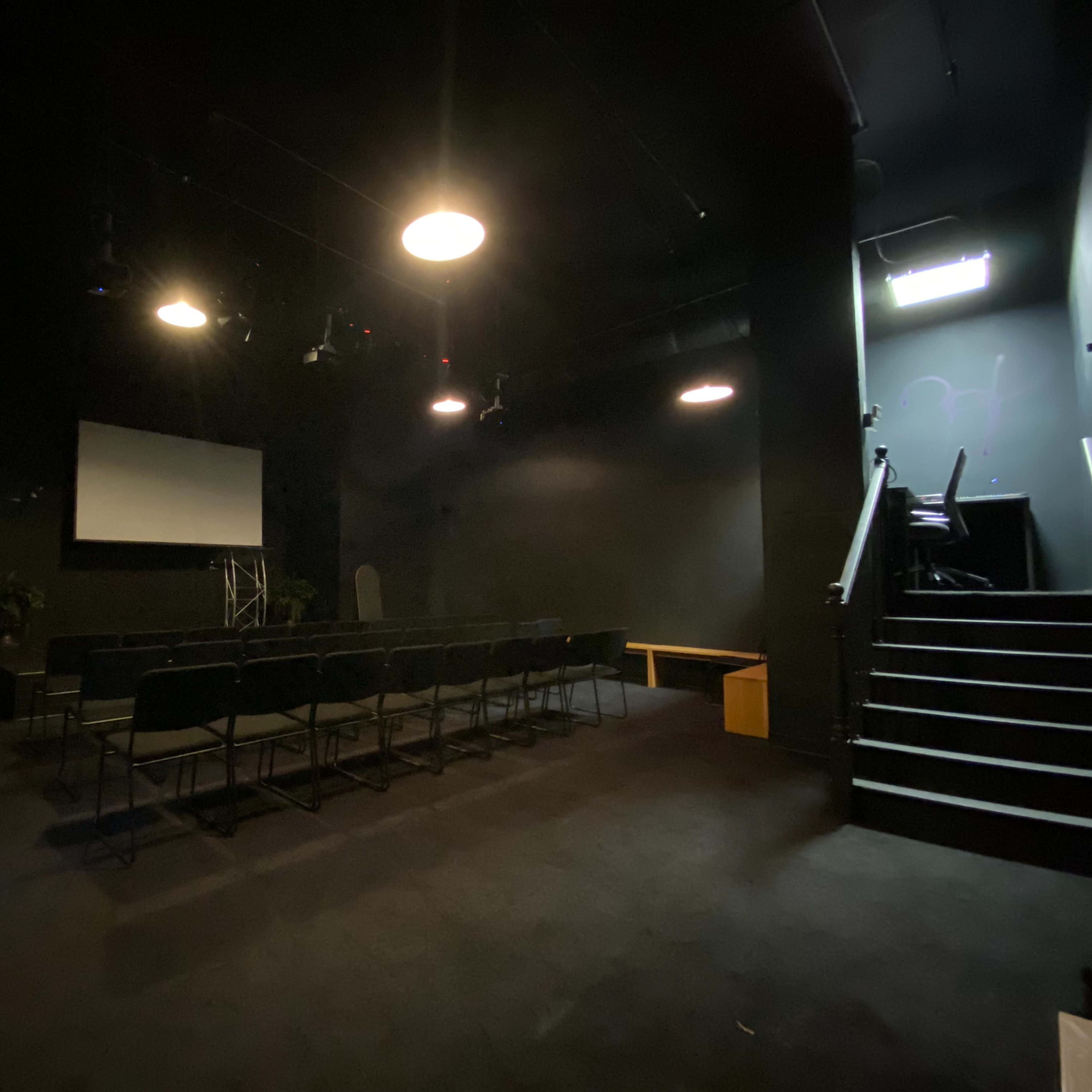 A dark room with a seating area, a screen at the front, and a staircase leading to an upper level.