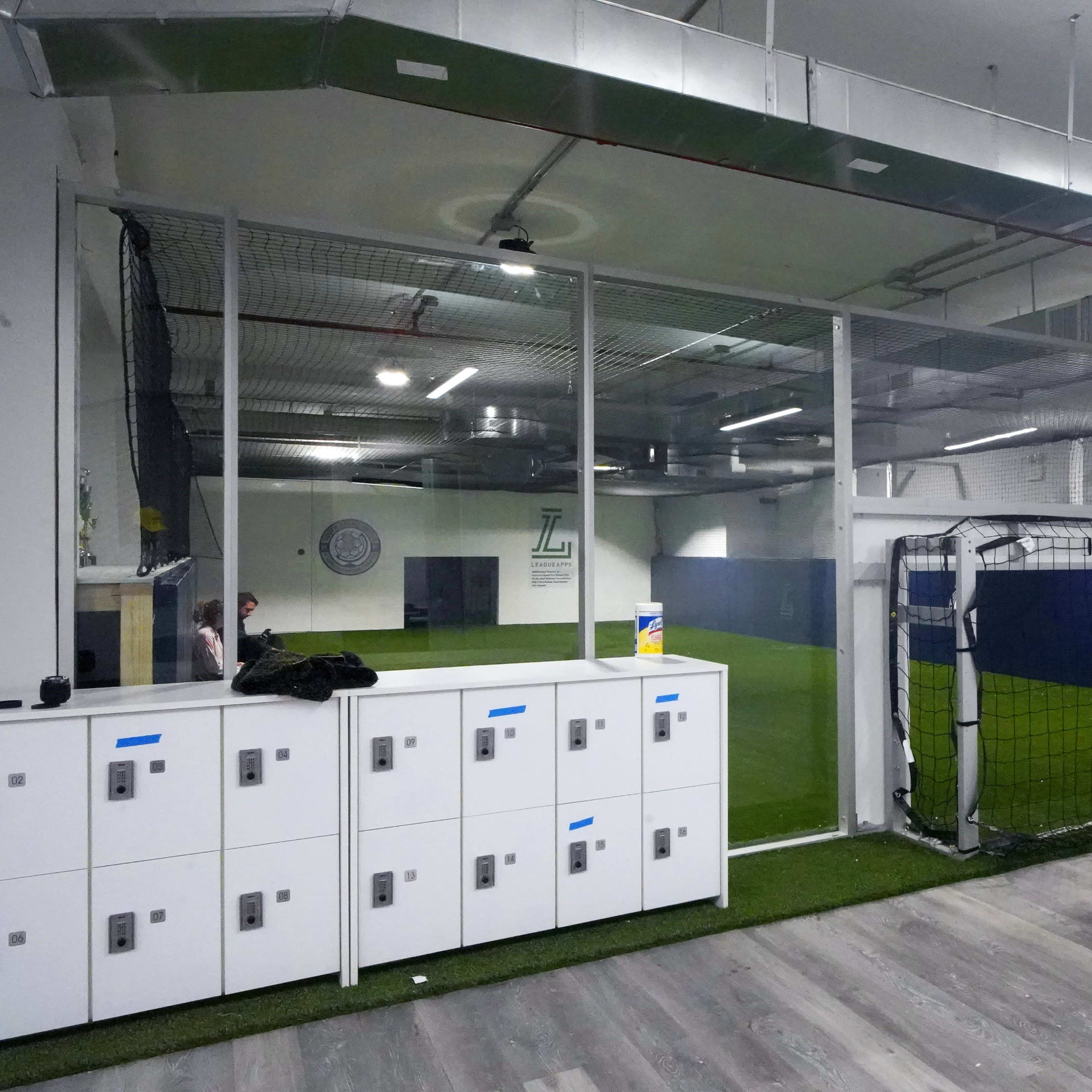 An indoor soccer facility with a small field, goalposts, and locker storage along one wall.