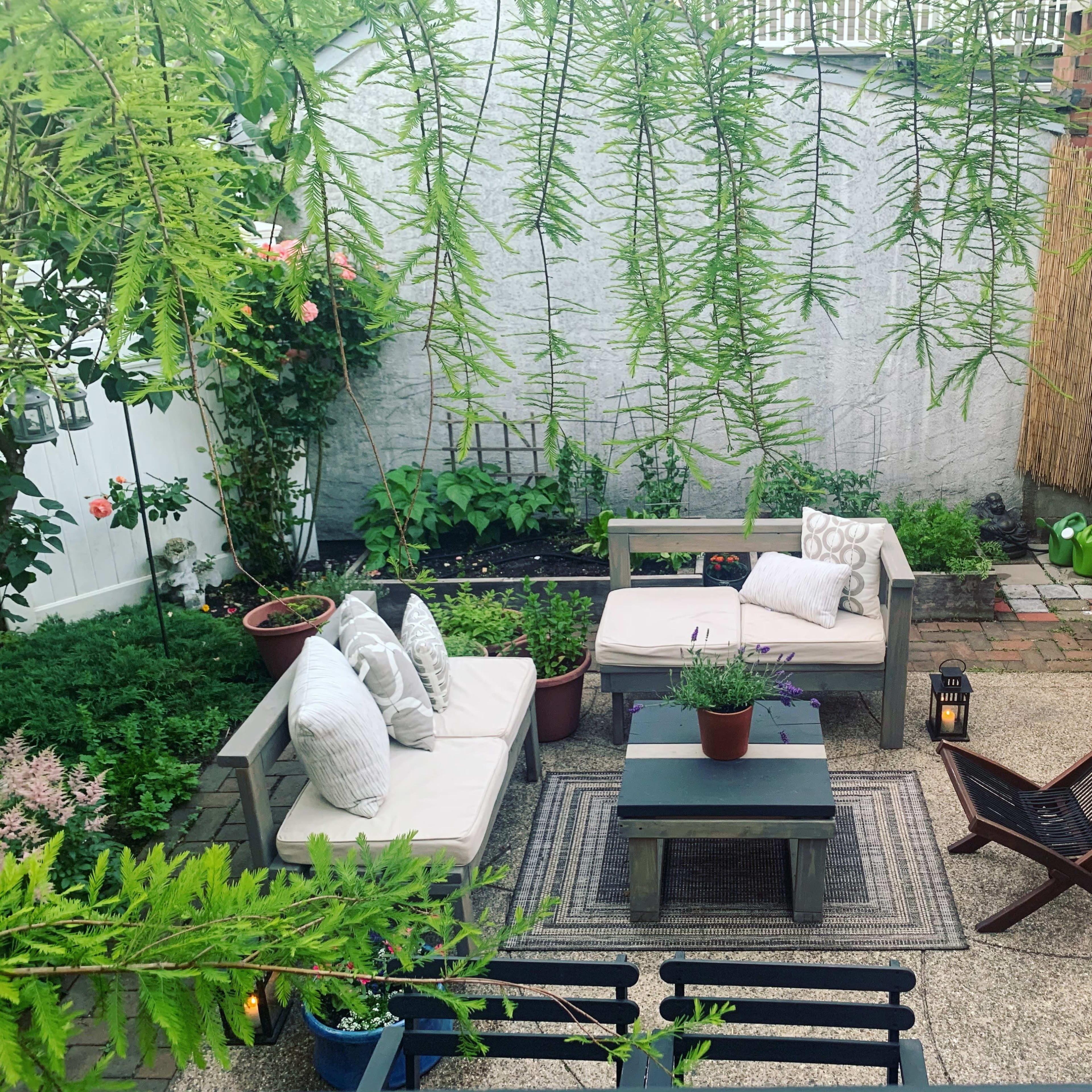 A small, well-maintained garden patio with seating arrangements, potted plants, and a barbecue area.