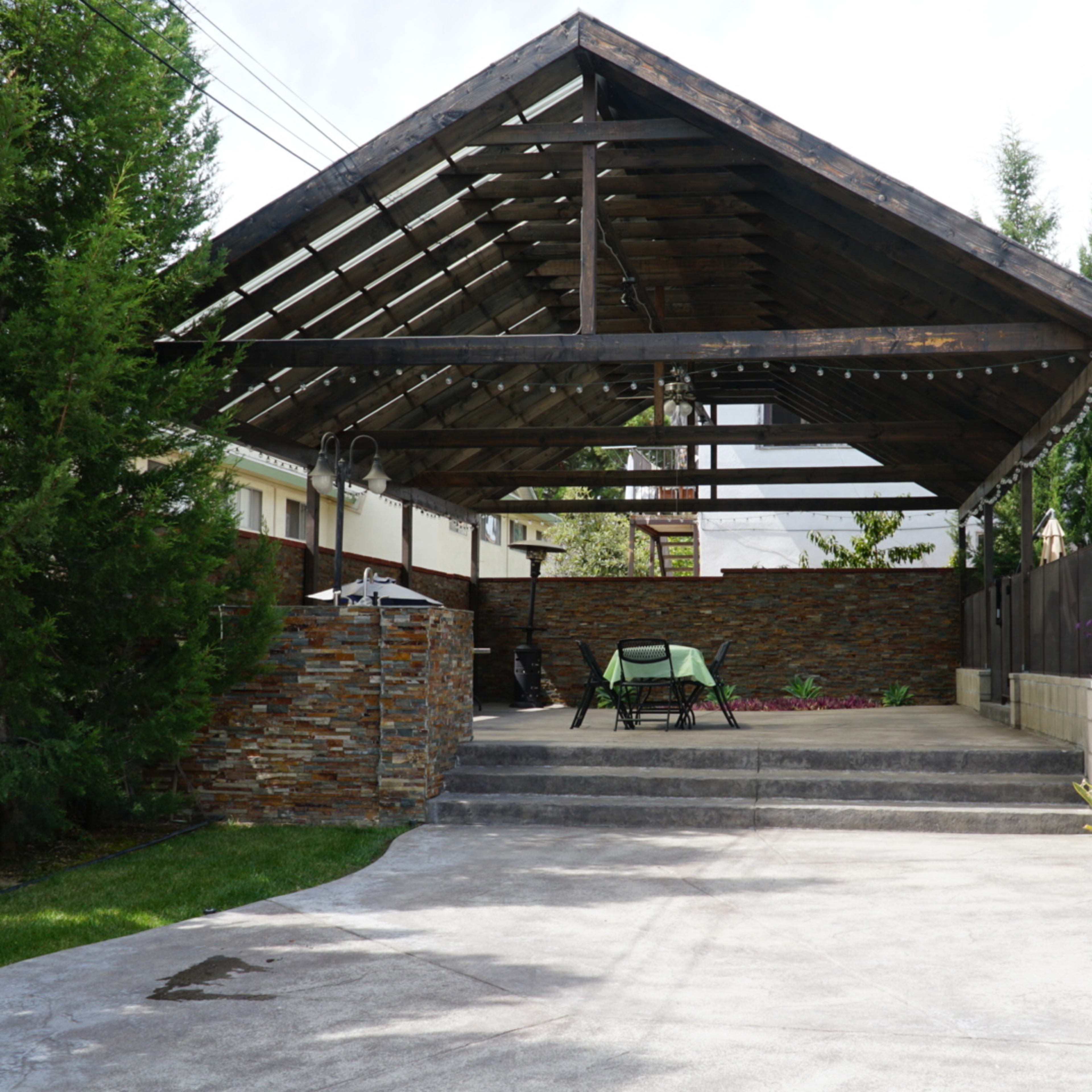 A covered outdoor patio features stone walls, a seating area, and landscaped greenery.