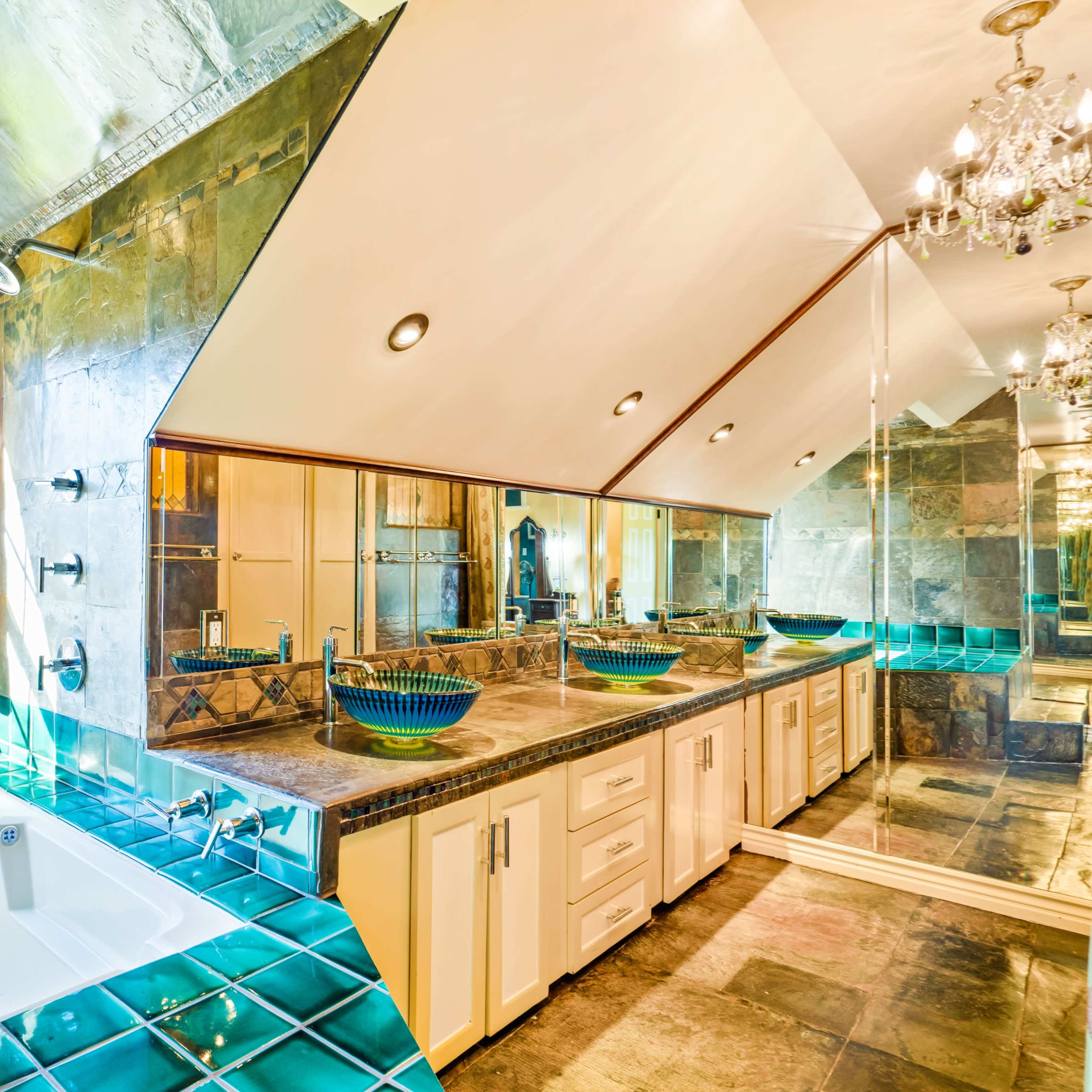 The bathroom features a spacious layout with a large window, double sinks under a mirrored wall, and a separate jetted tub with turquoise tile accents.