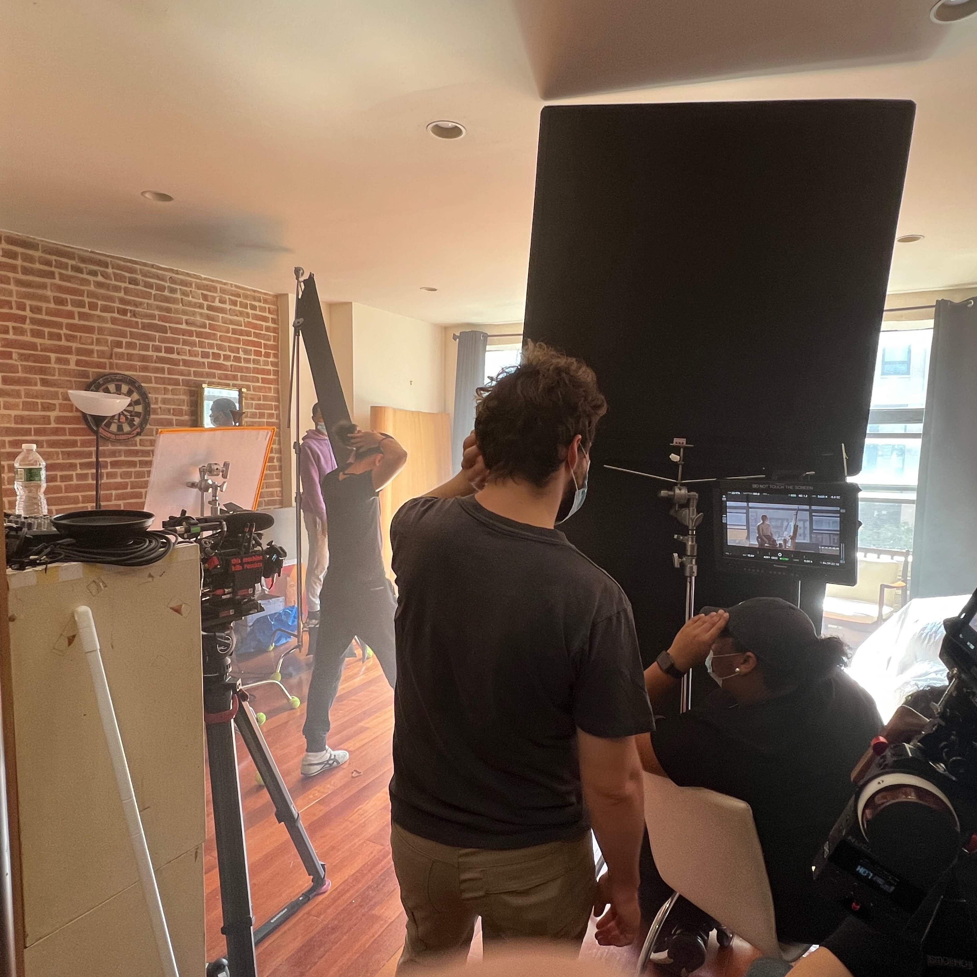 A crew sets up filming equipment in a spacious apartment with a brick wall and large windows.
