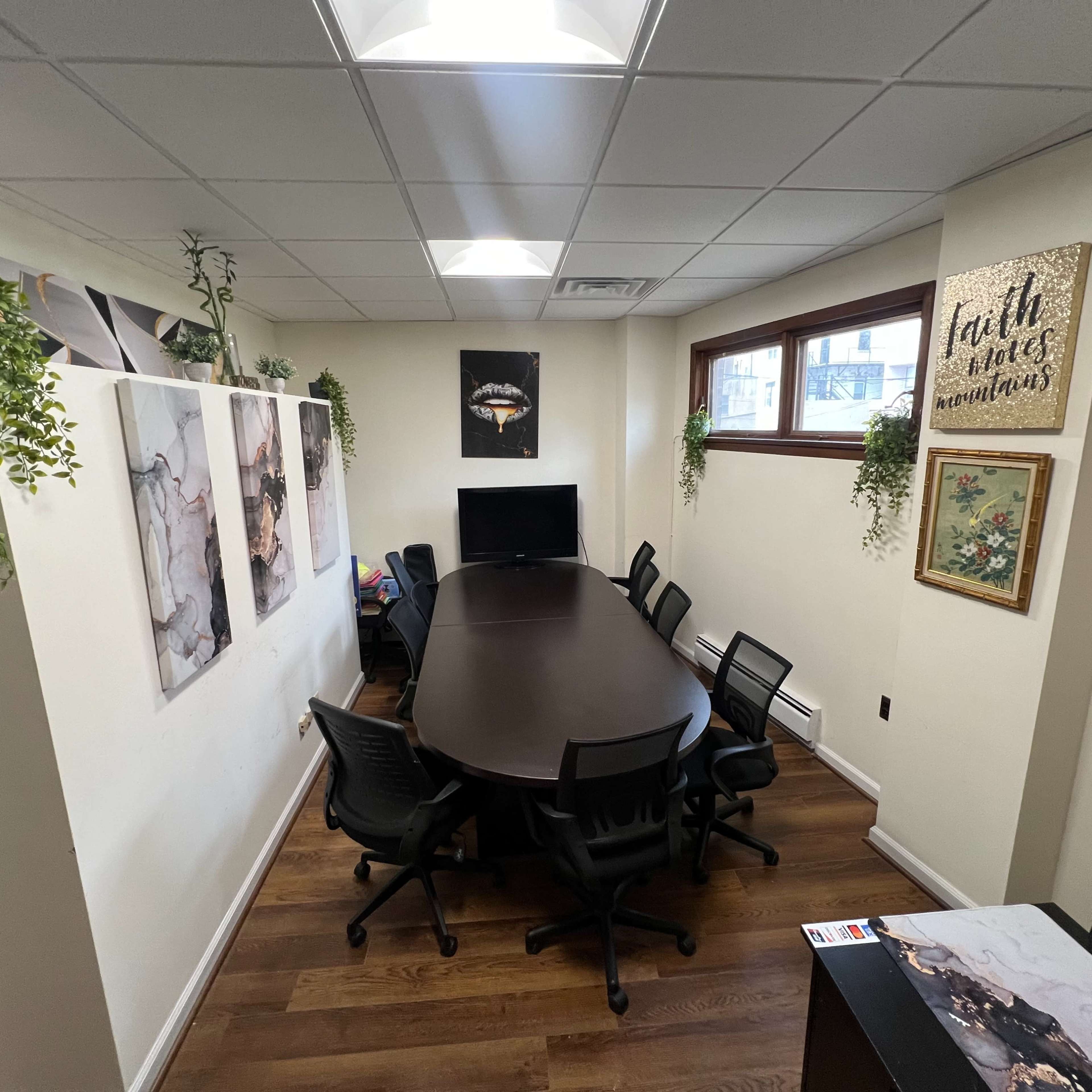 A conference room with a large oval table surrounded by black chairs, decorated with wall art and plants.