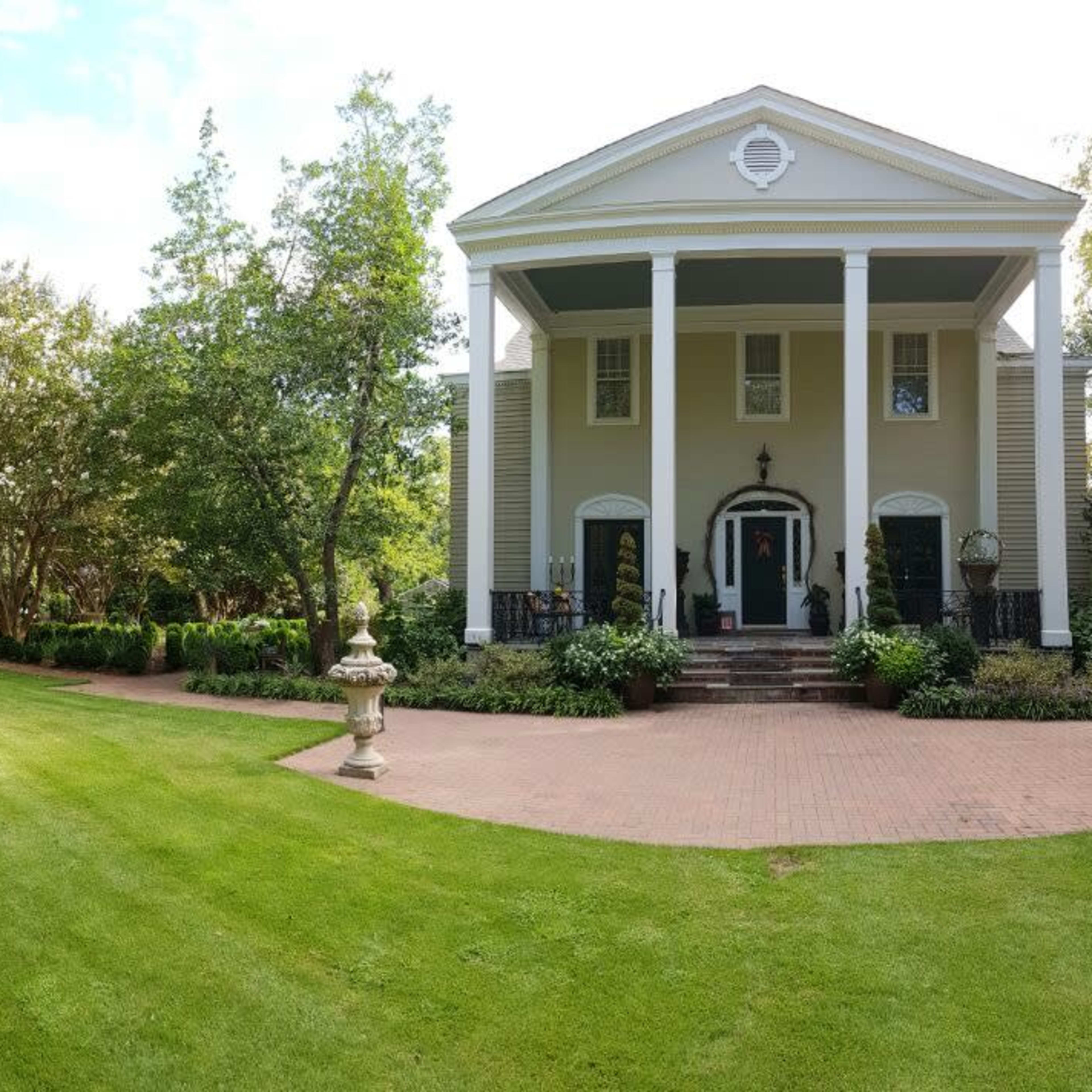 A well-maintained garden area next to a large, two-story house with a covered porch.