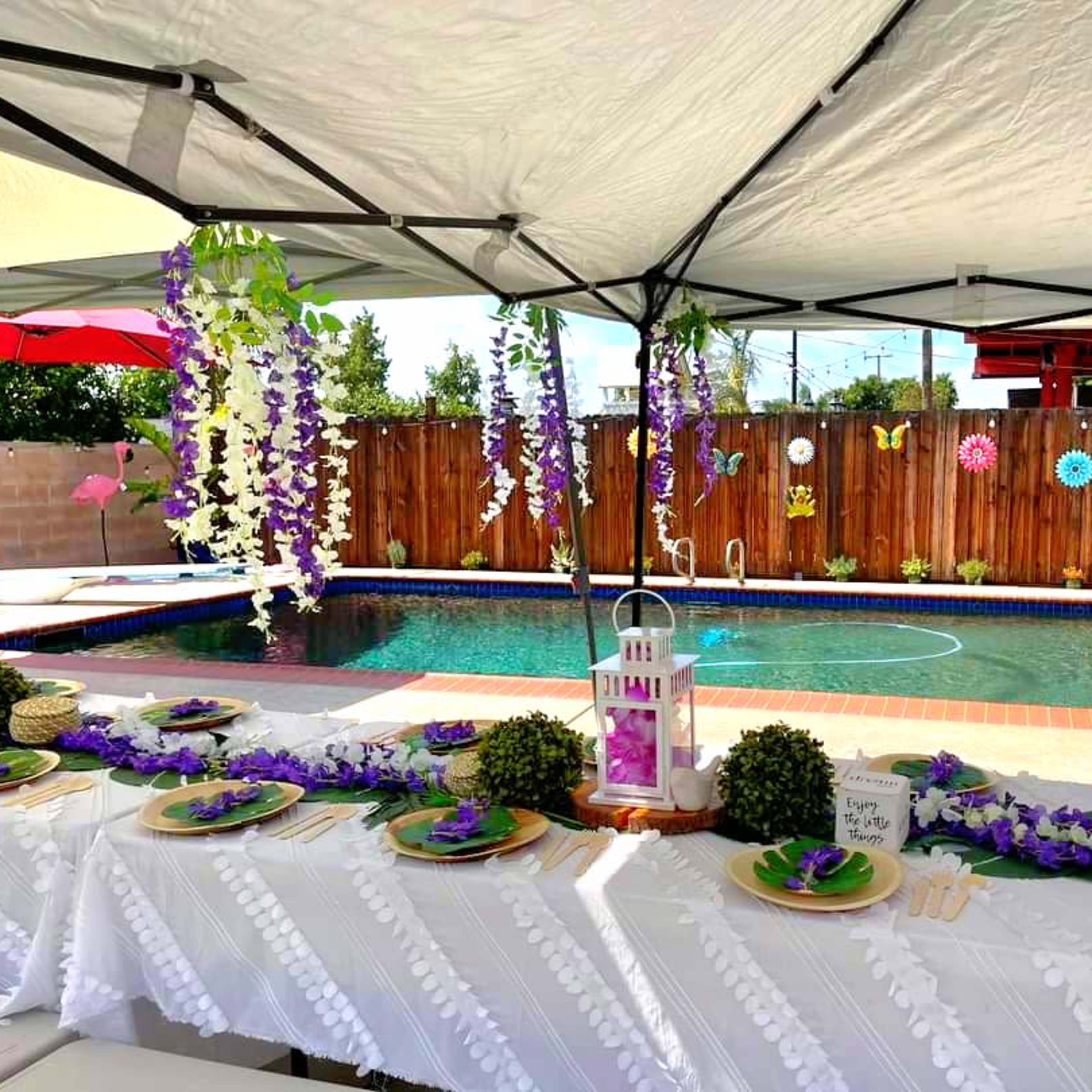 A backyard scene features a decorated table under a canopy, with a pool in the background adorned with colorful decorations and a float.