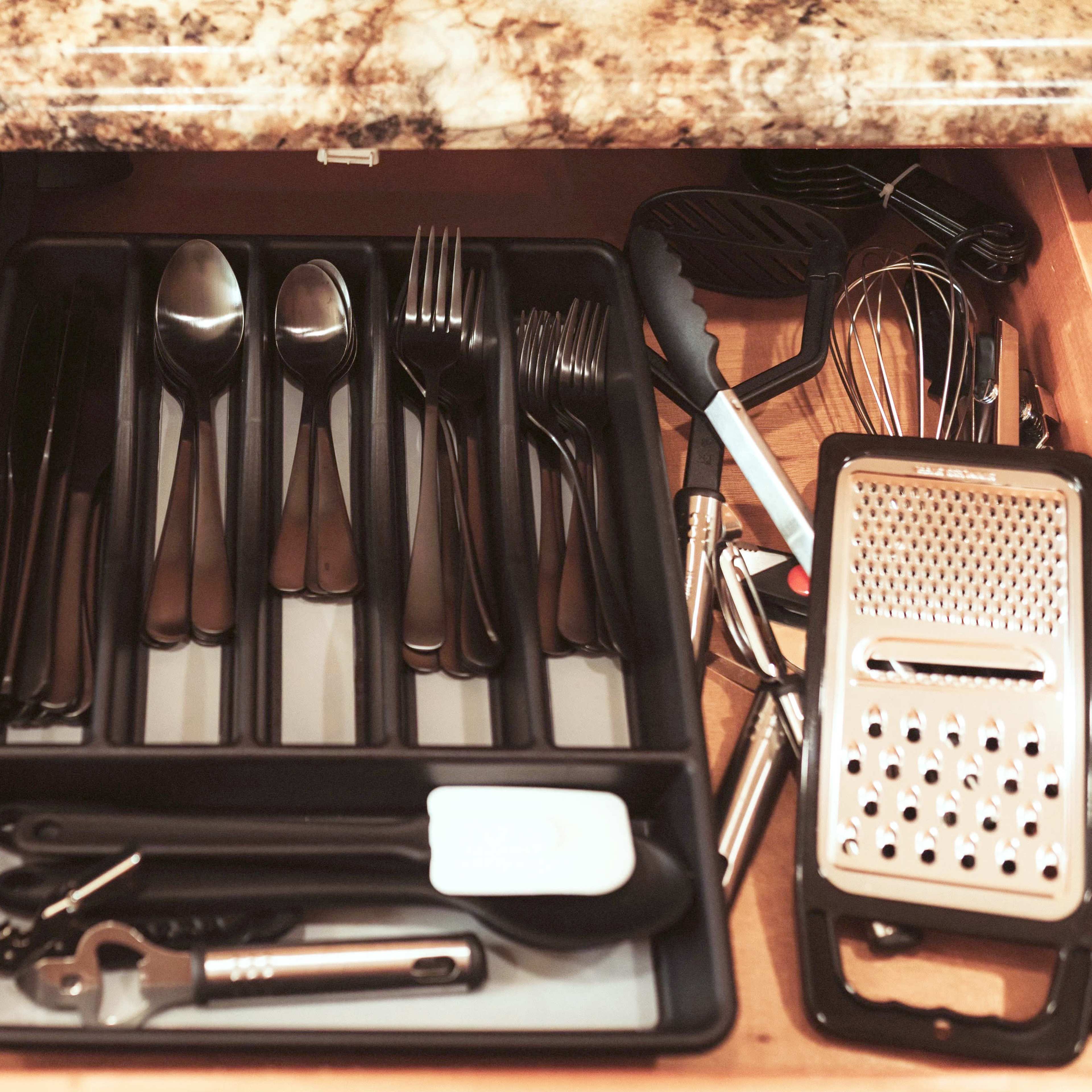 A kitchen drawer filled with neatly arranged utensils, including black plastic spatulas, metal spoons, forks, and a grater.