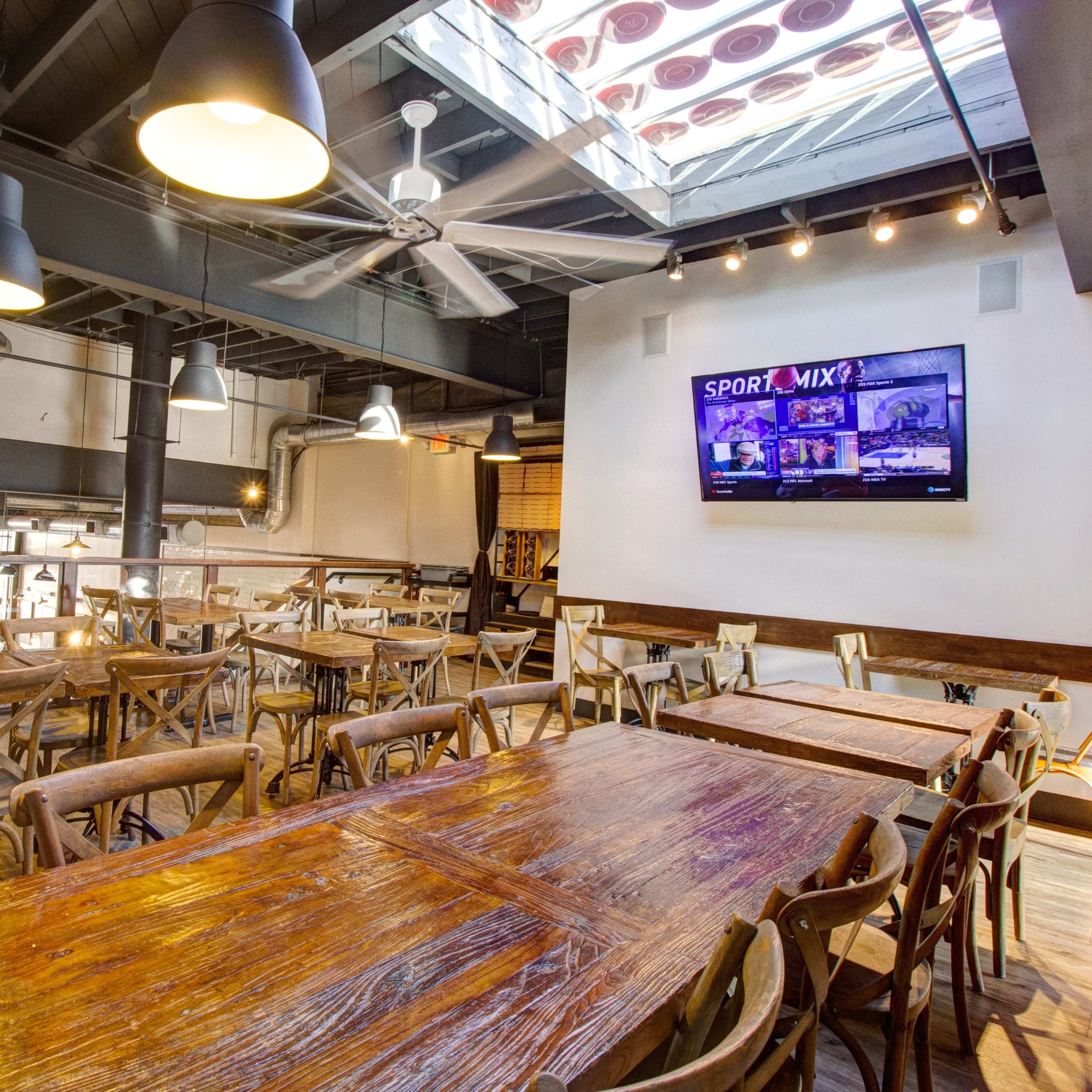 A spacious restaurant interior with wooden tables and a large screen displaying content on a white wall.