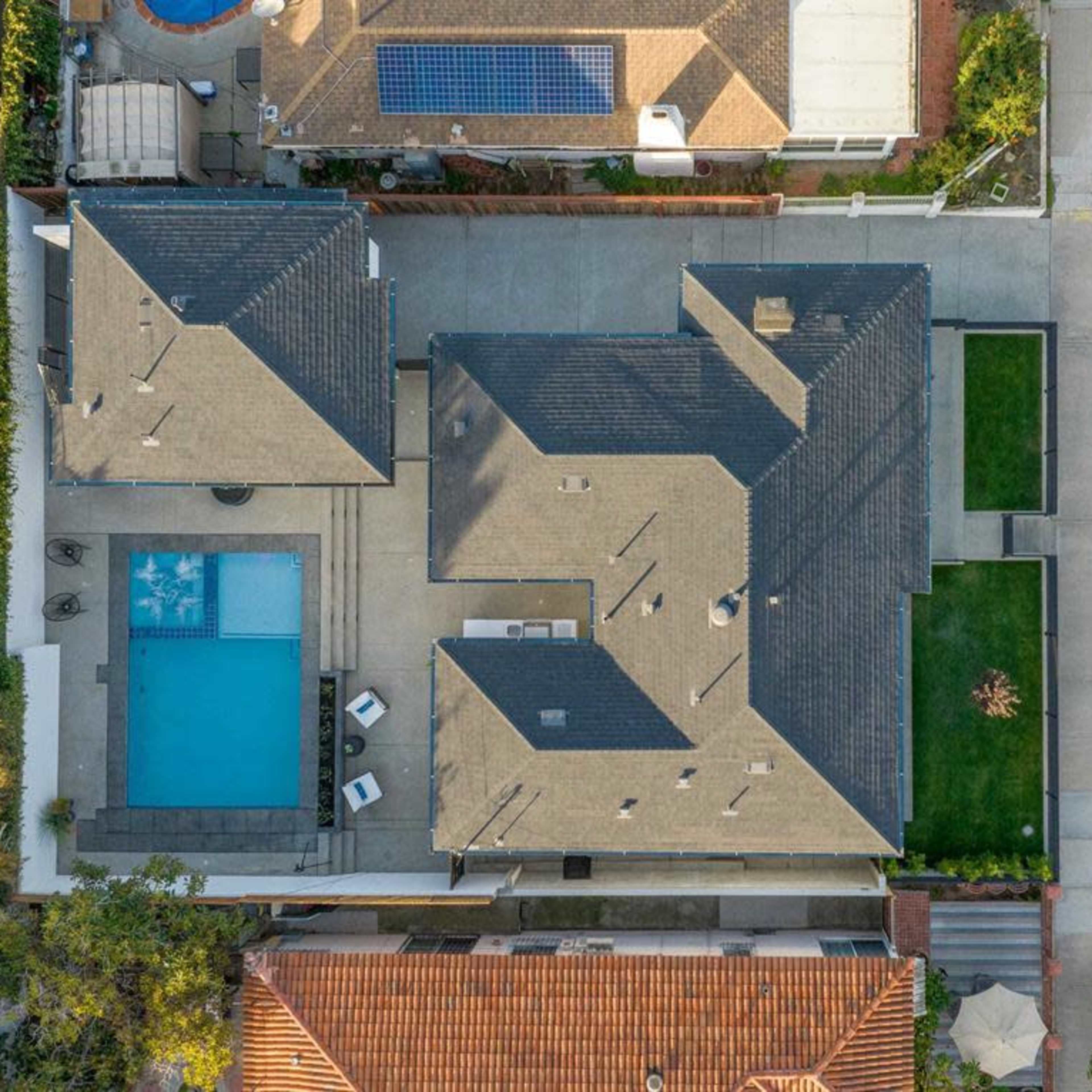 A bird's-eye view of a residential property featuring a swimming pool, landscaped yard, and several adjacent houses.