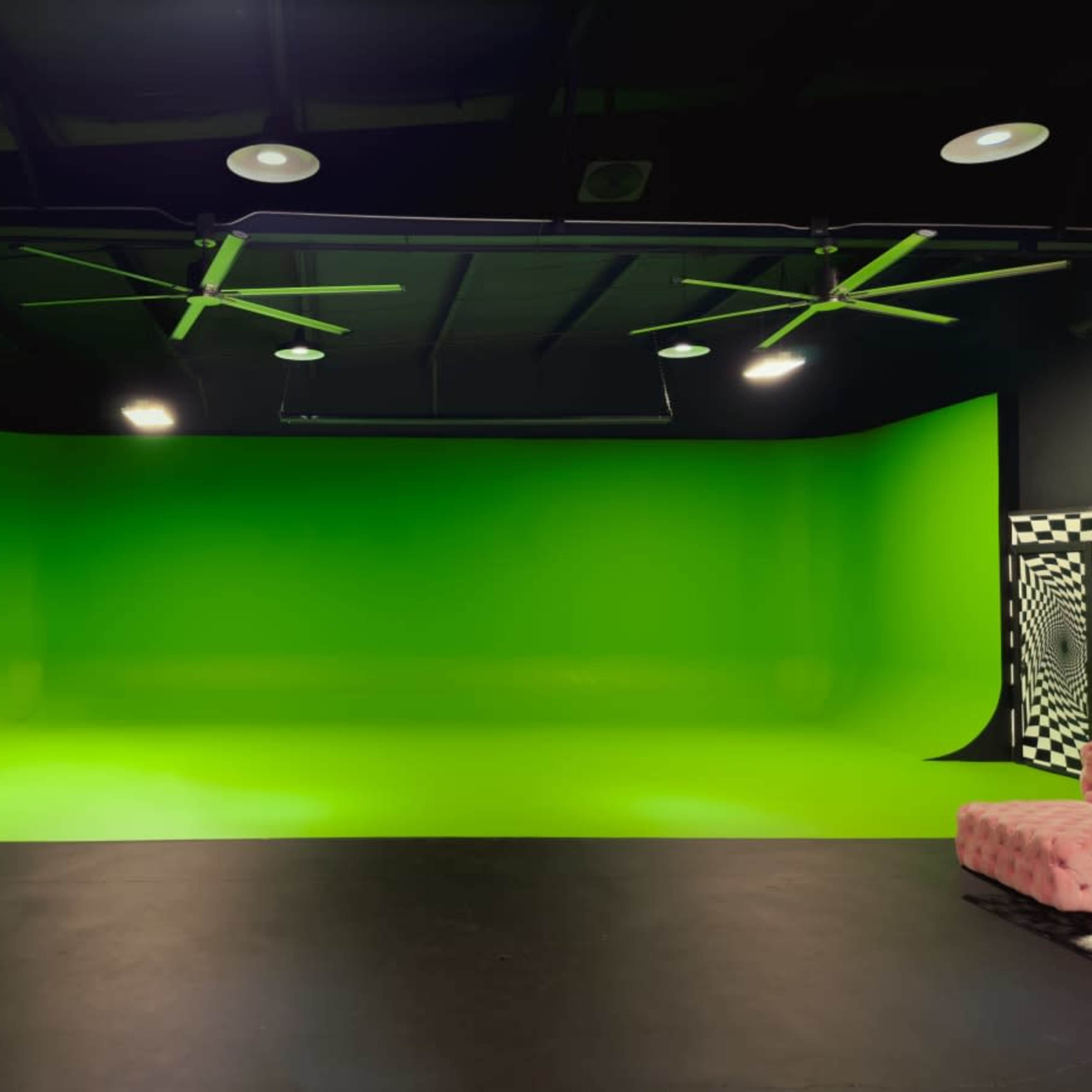 A studio with a bright green backdrop, black flooring, and ceiling fans, along with a pink couch in the corner.
