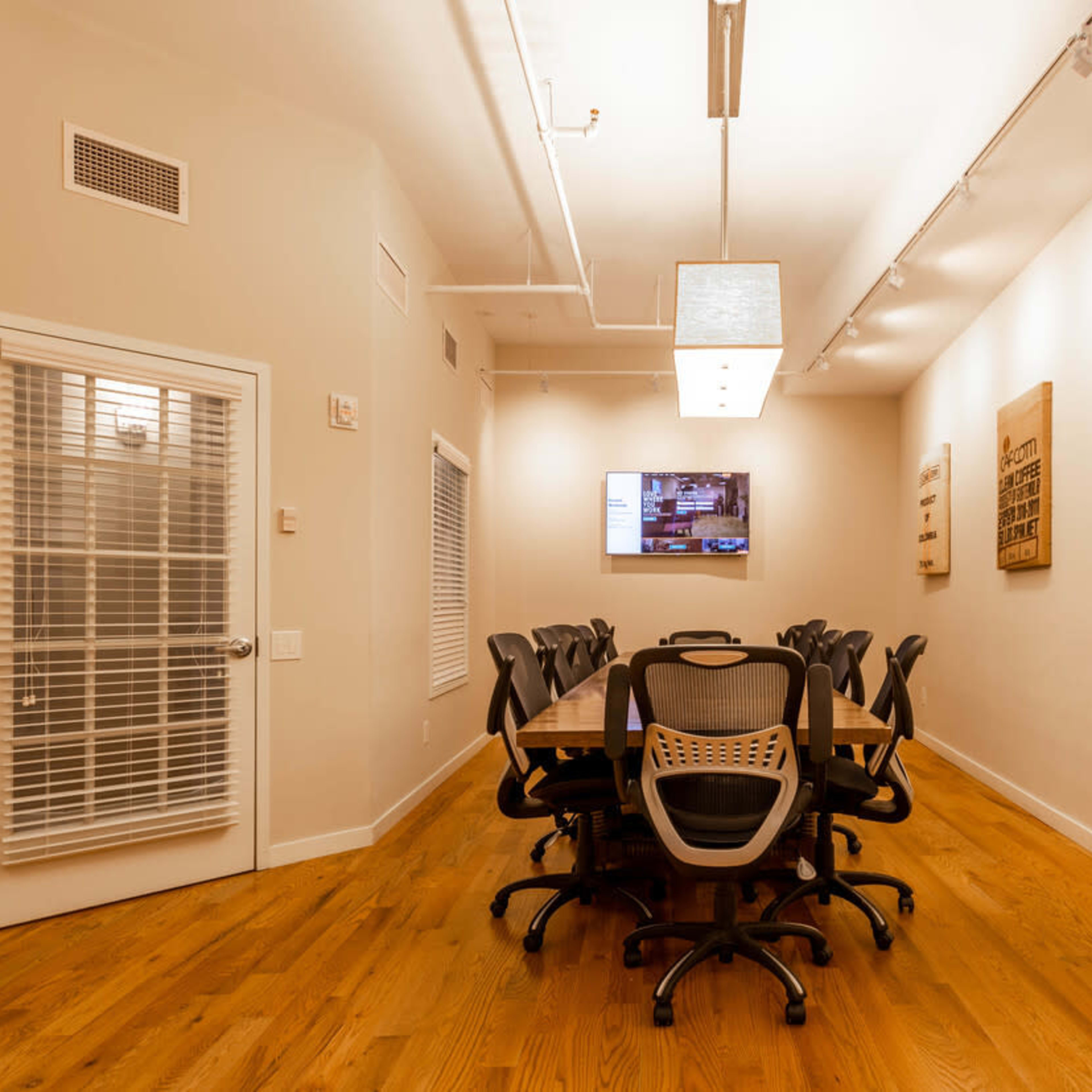 A conference room with a long wooden table, several black office chairs, a television mounted on the wall, and decorative wall art.
