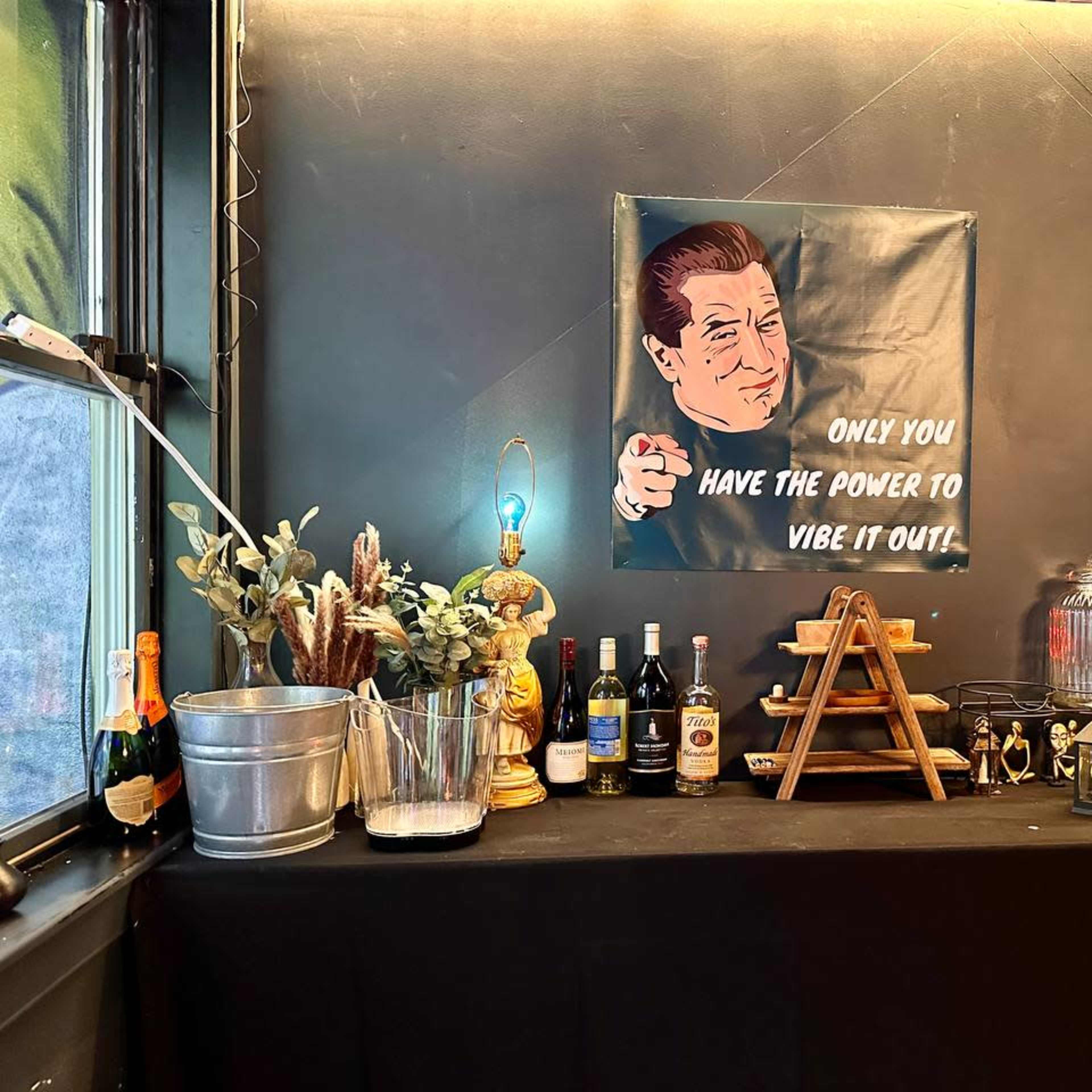 A bar setup with various bottles of liquor, a champagne bucket, and a framed poster with the text "ONLY YOU HAVE THE POWER TO VIBE IT OUT."