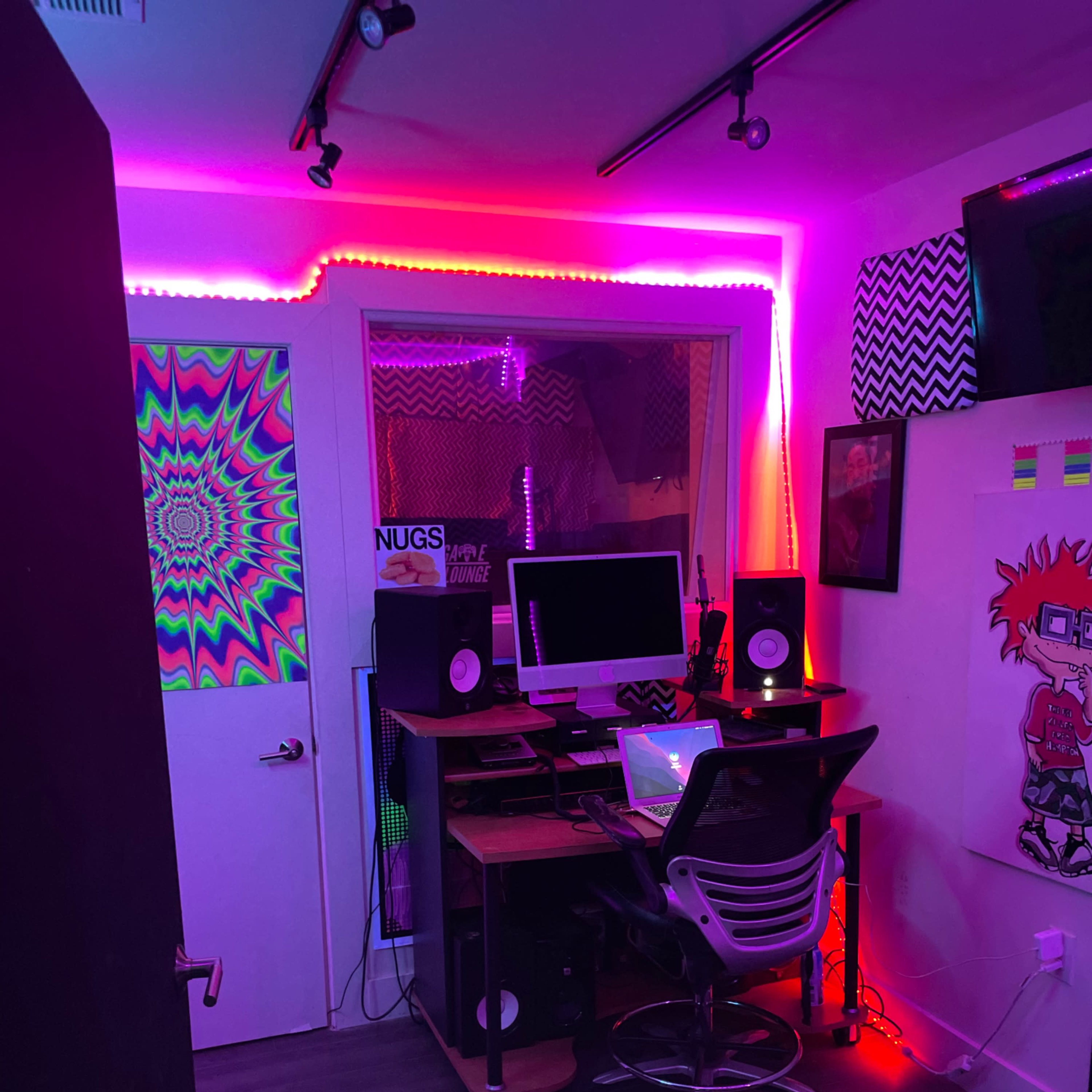 A music production studio with colorful LED lights, a computer setup, and sound equipment against a wall decorated with vibrant art.