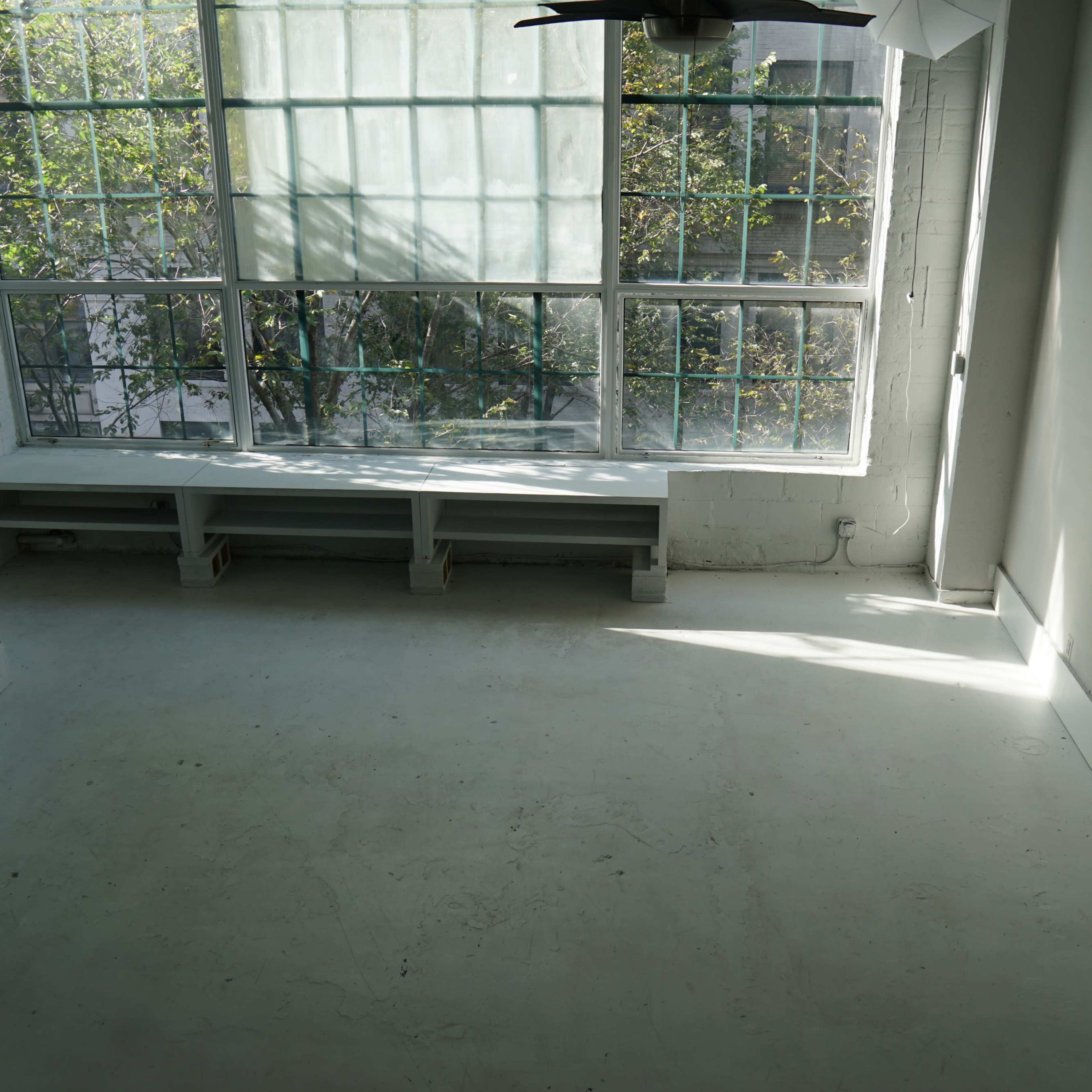 A spacious, empty room with large windows allowing natural light to enter and a mirrored wall on one side.