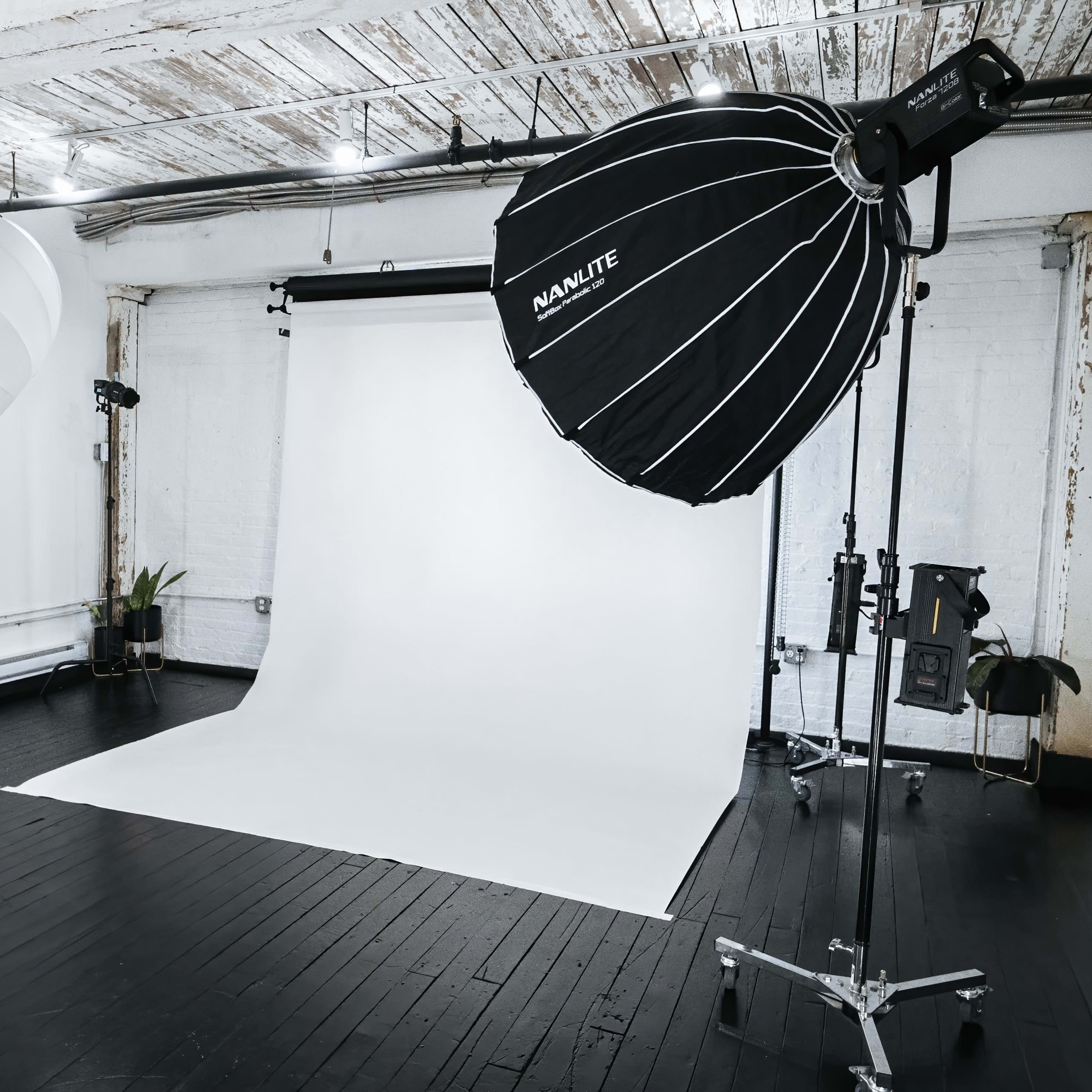 A photography studio equipped with two large softbox lights and a plain white backdrop on a wooden floor.