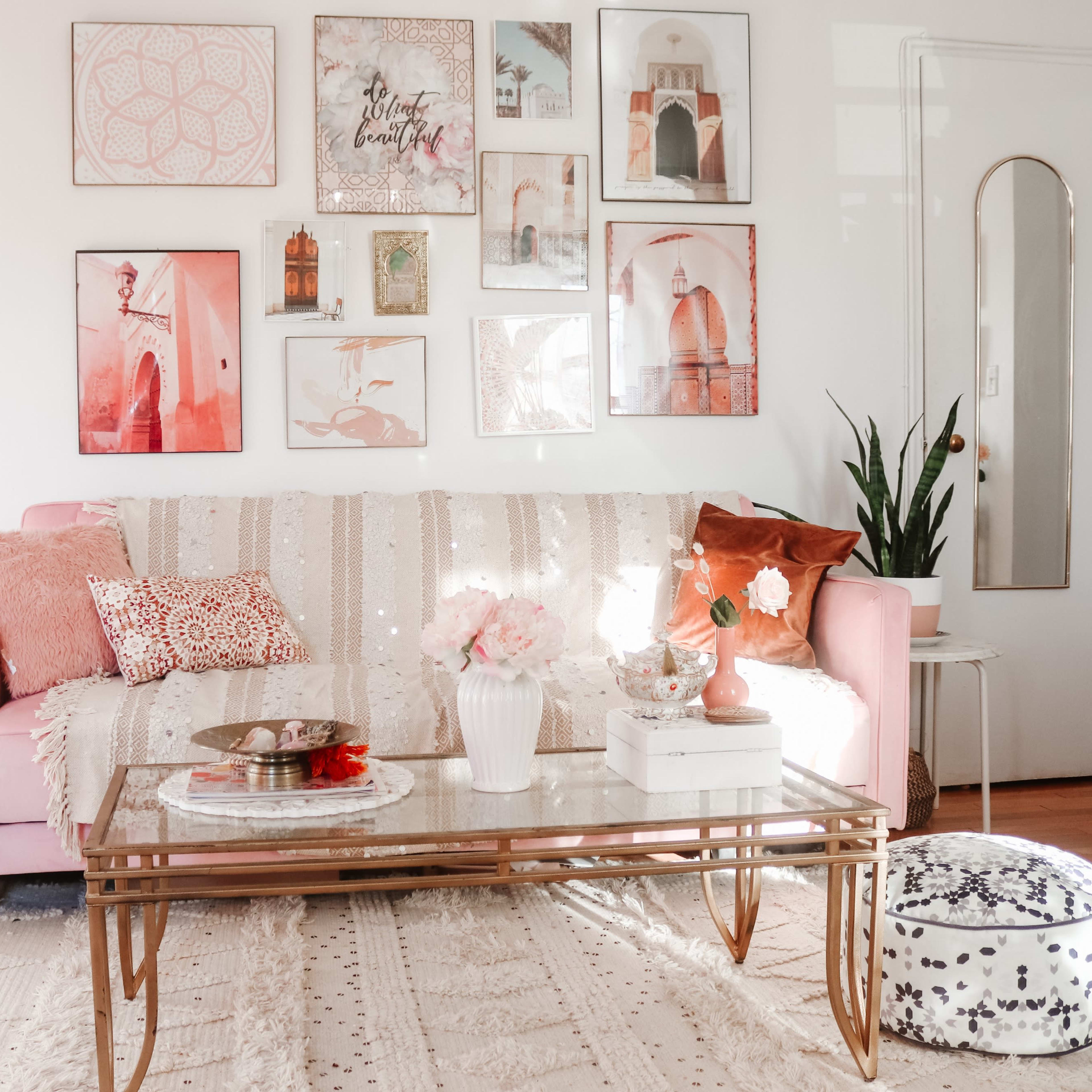 A well-decorated living room features a pink sofa with various decorative pillows, a glass coffee table, and artwork on the walls.