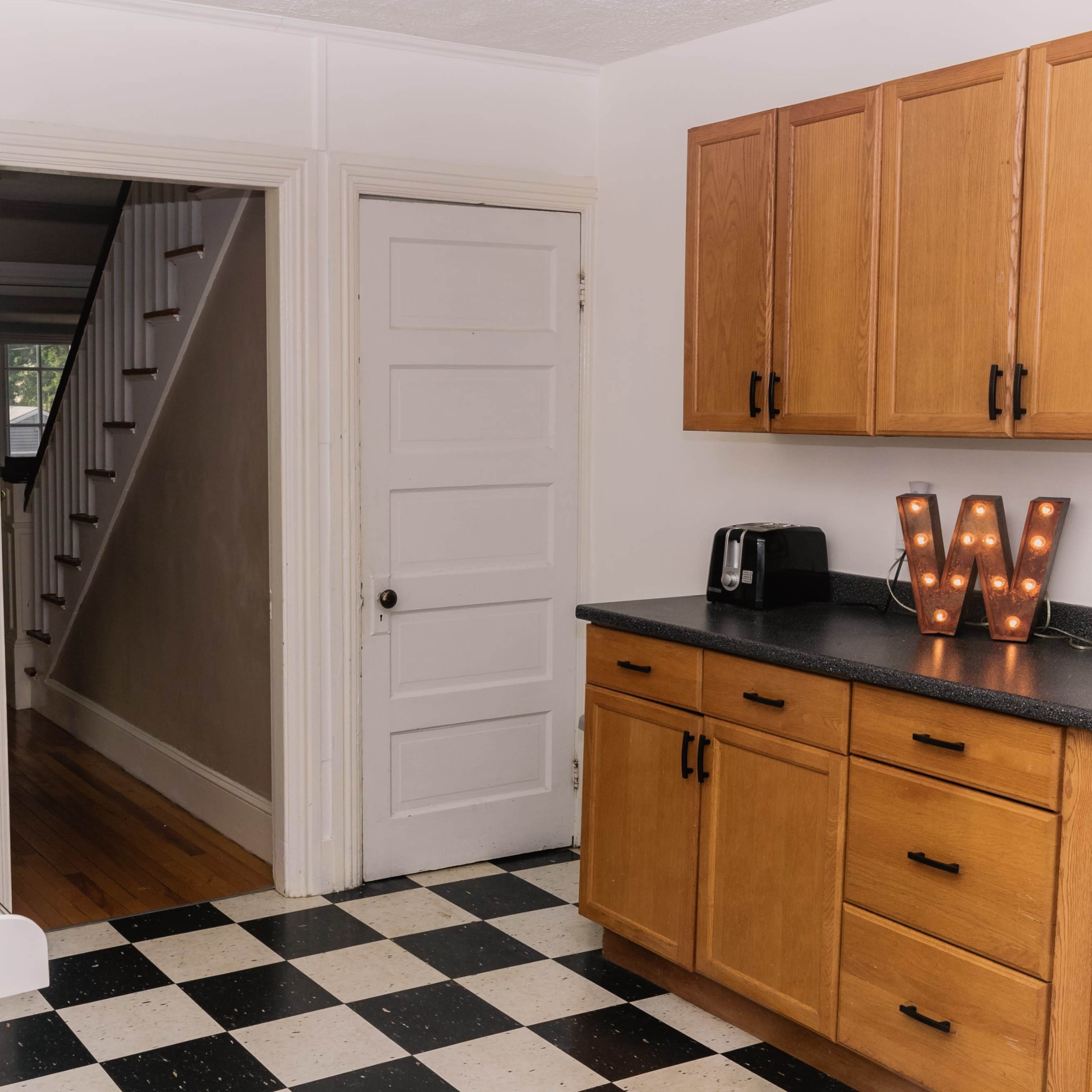 A kitchen with wooden cabinets, a white stove, and a doorway leading to a hallway with a staircase.