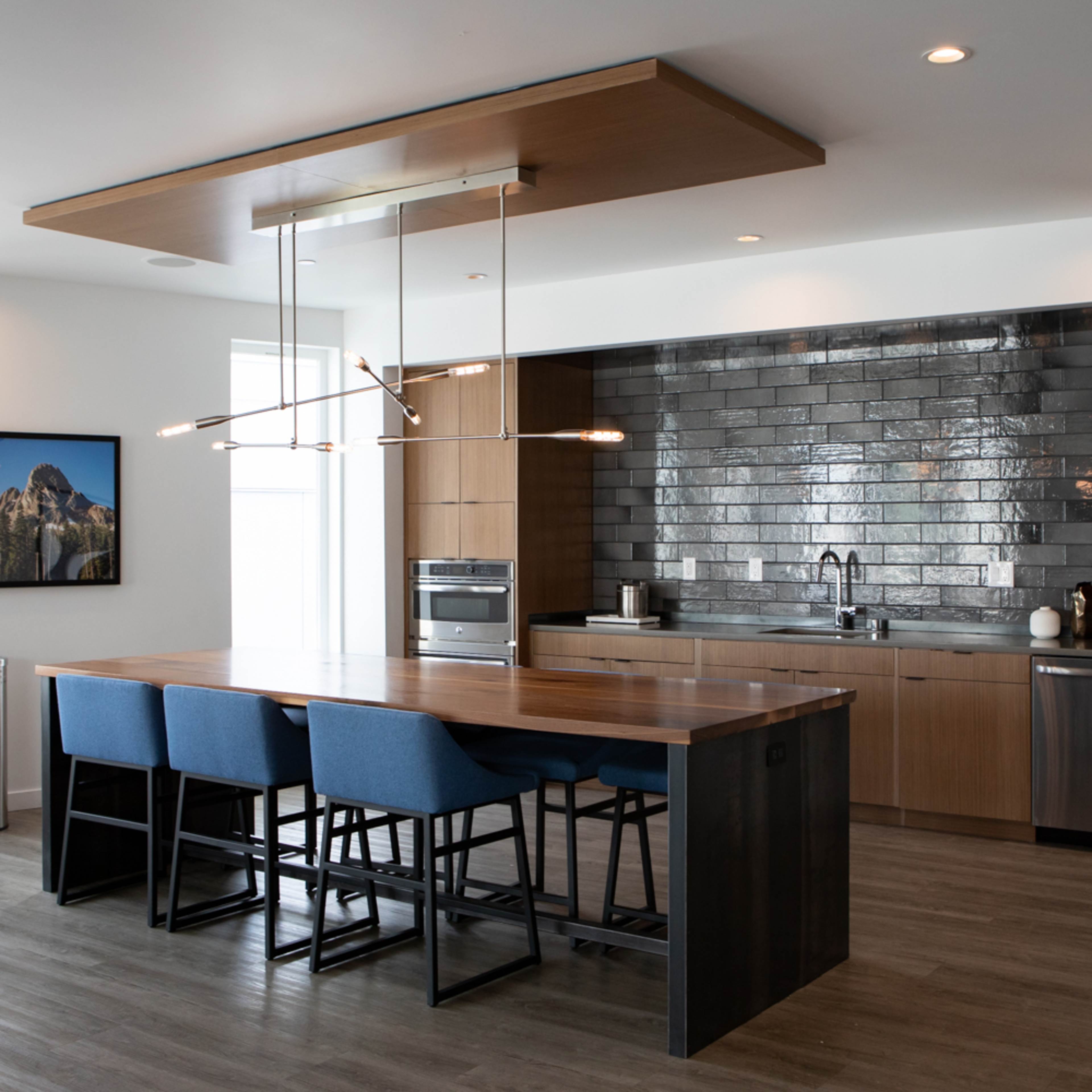 A modern kitchen featuring a wooden island with blue bar stools, stainless steel appliances, and a tiled backsplash.