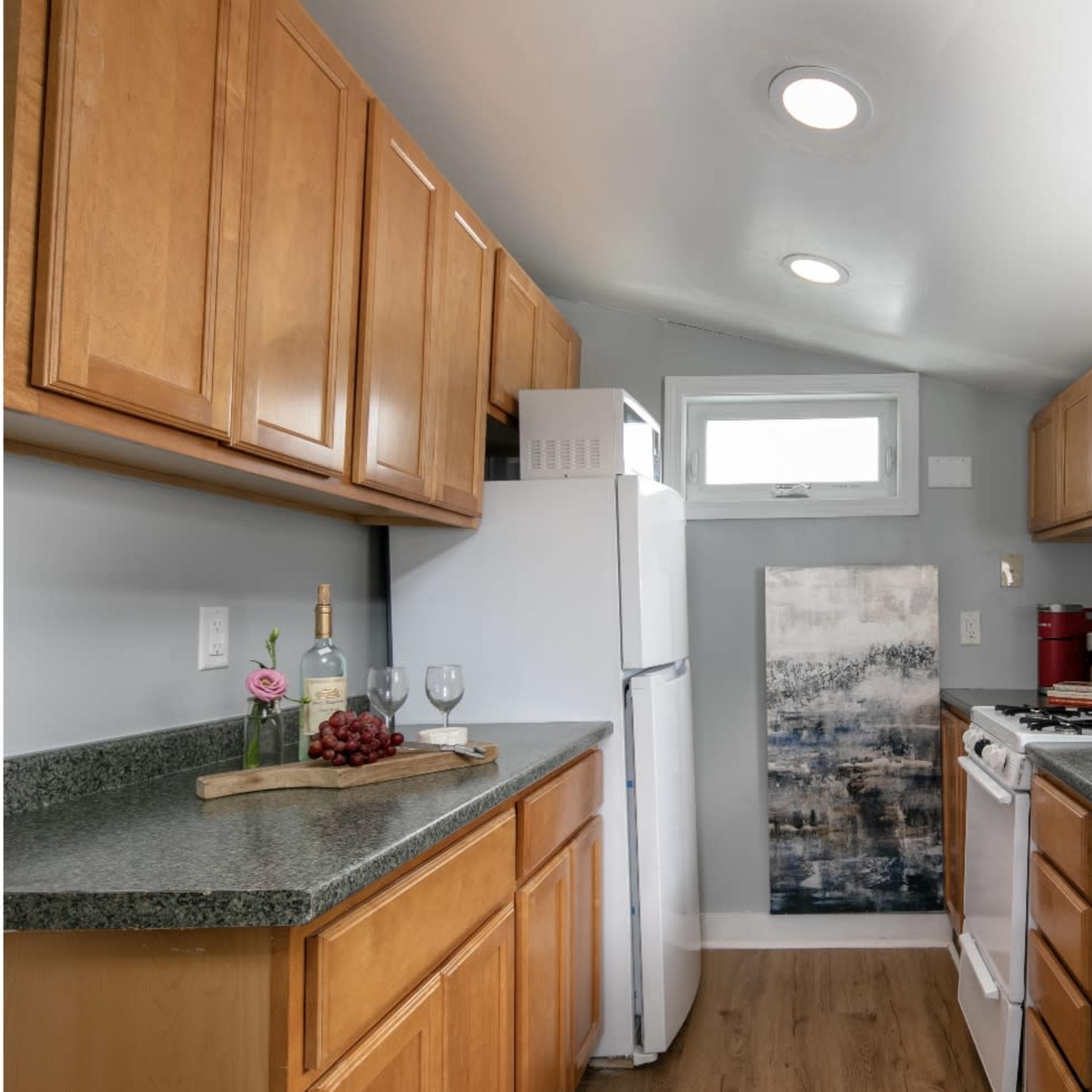 A compact kitchen with wooden cabinets, a refrigerator, a stove, and a small dining area featuring a bottle of wine and glasses on the counter.