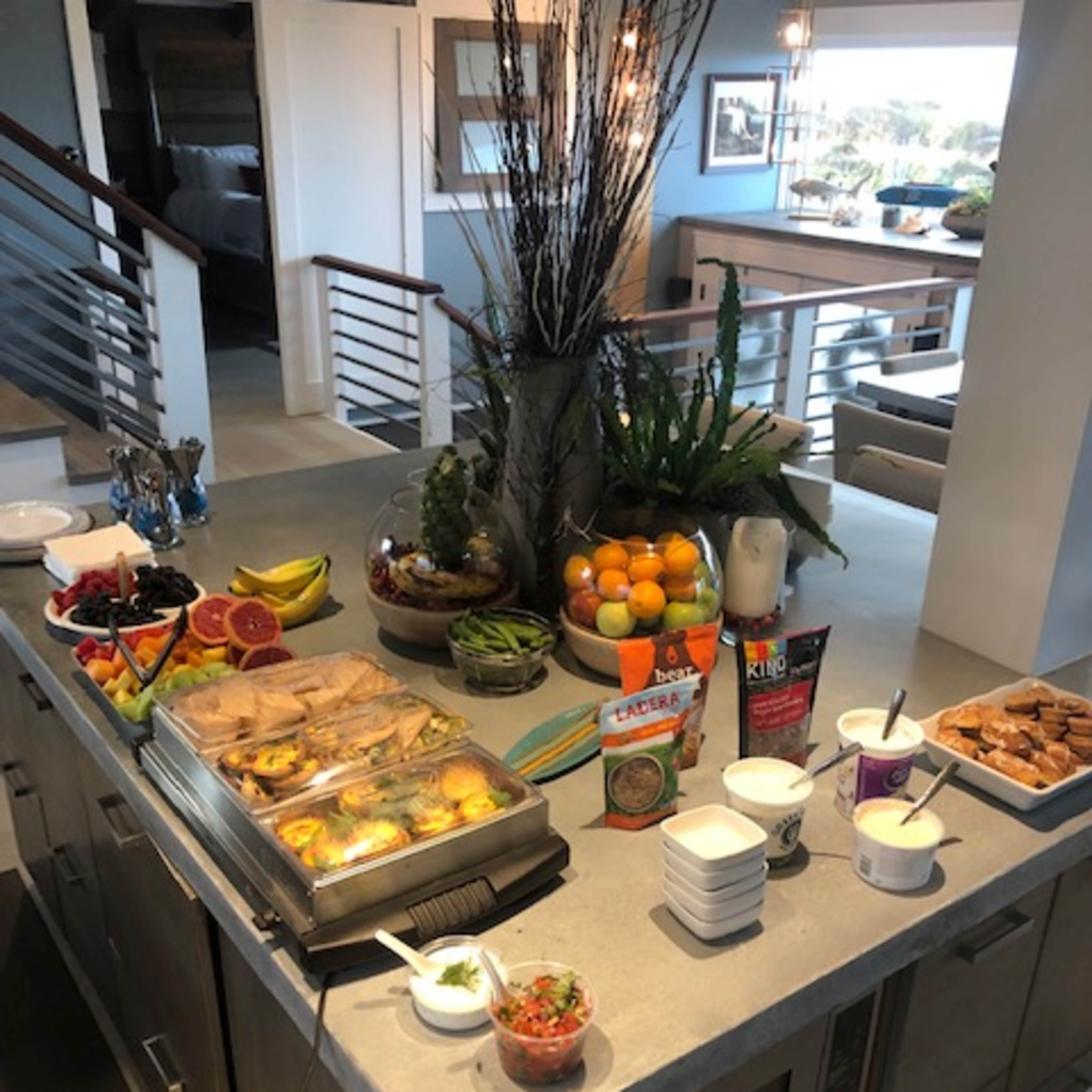 A large kitchen island is laden with a variety of food items, including pastries, fruits, yogurt, and dips, arranged neatly in bowls and trays.