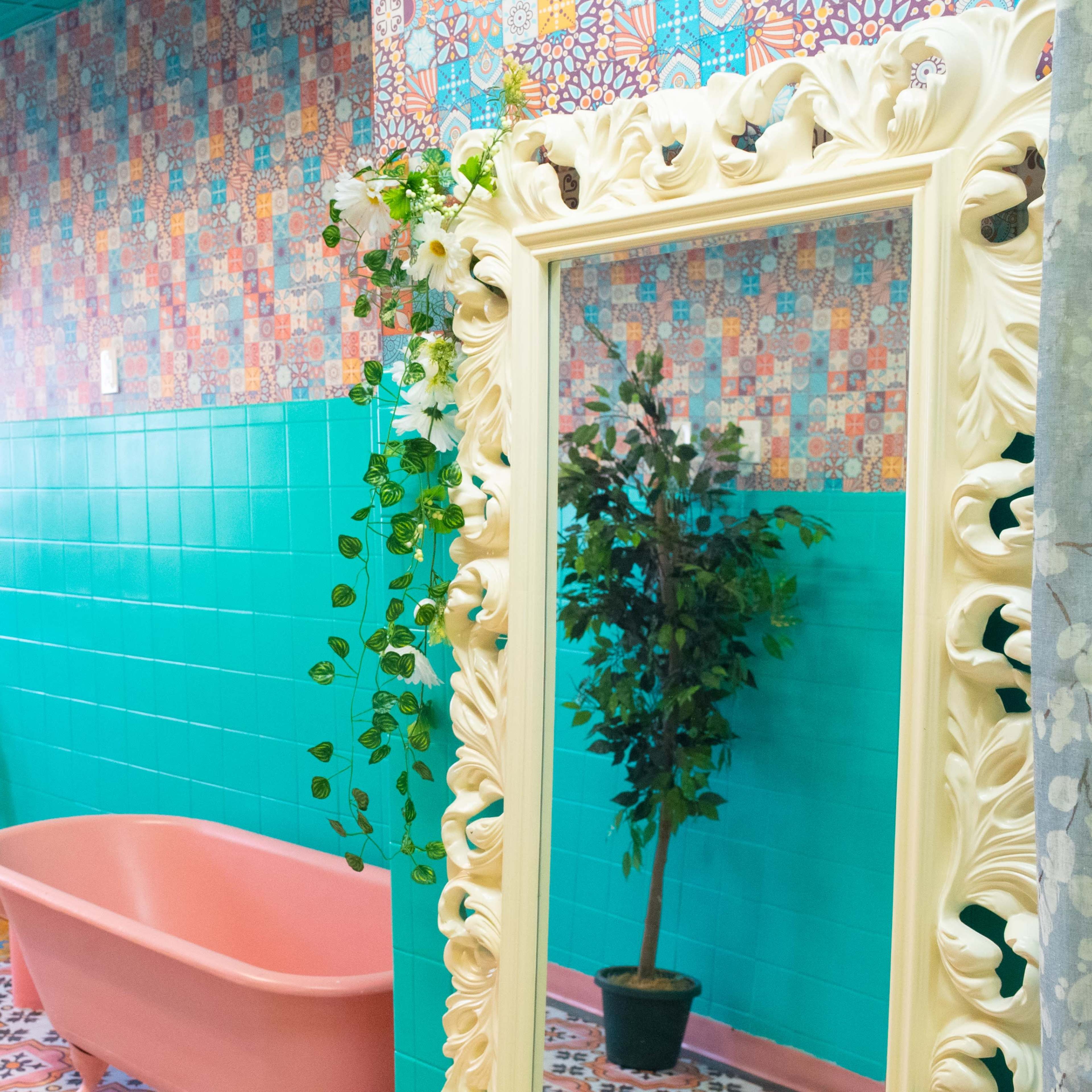 A colorful bathroom featuring a pink bathtub, ornate mirrors, and vibrant patterned tiles on the walls and floor.