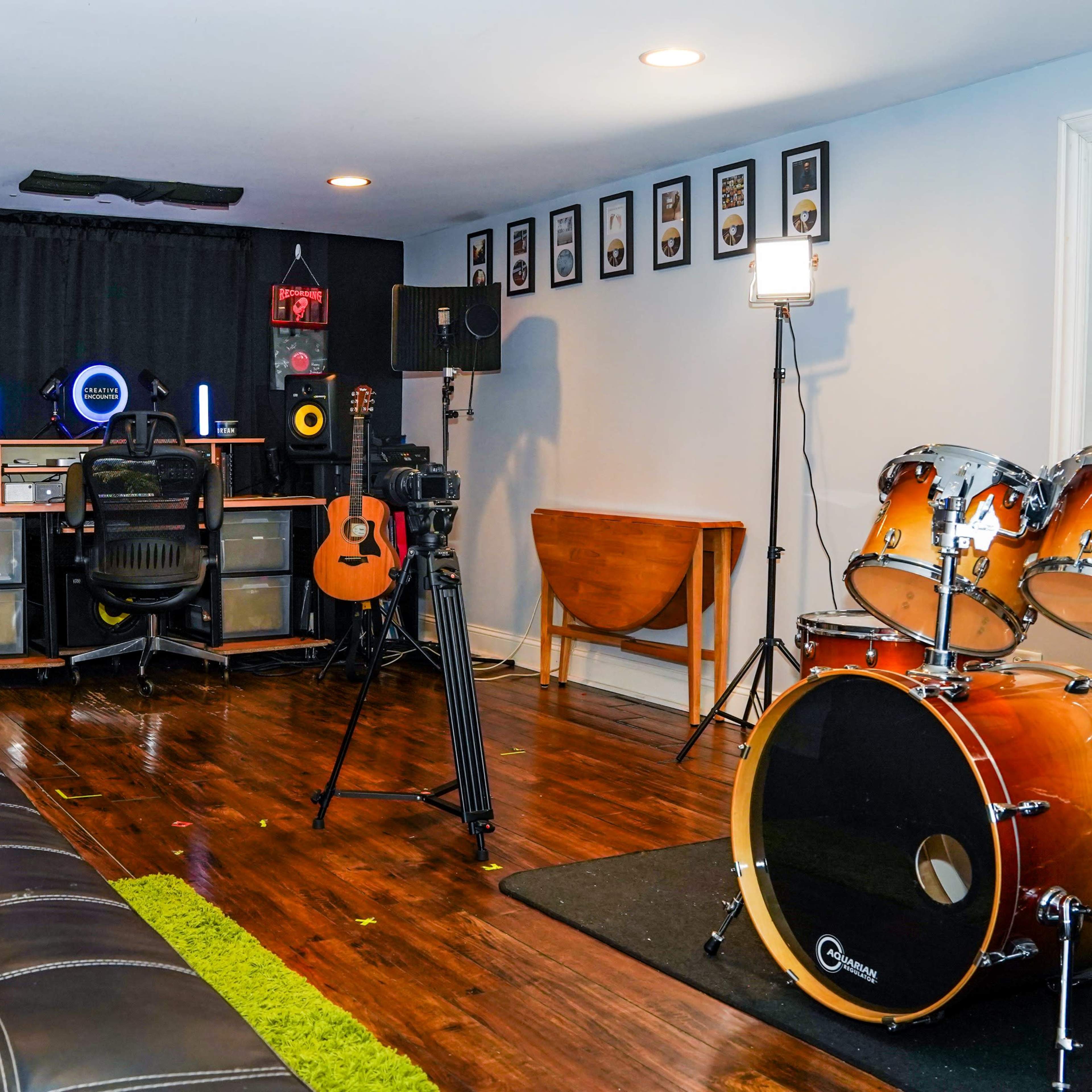 A home recording studio with guitars, a drum set, and a desk equipped with studio monitors and a microphone.