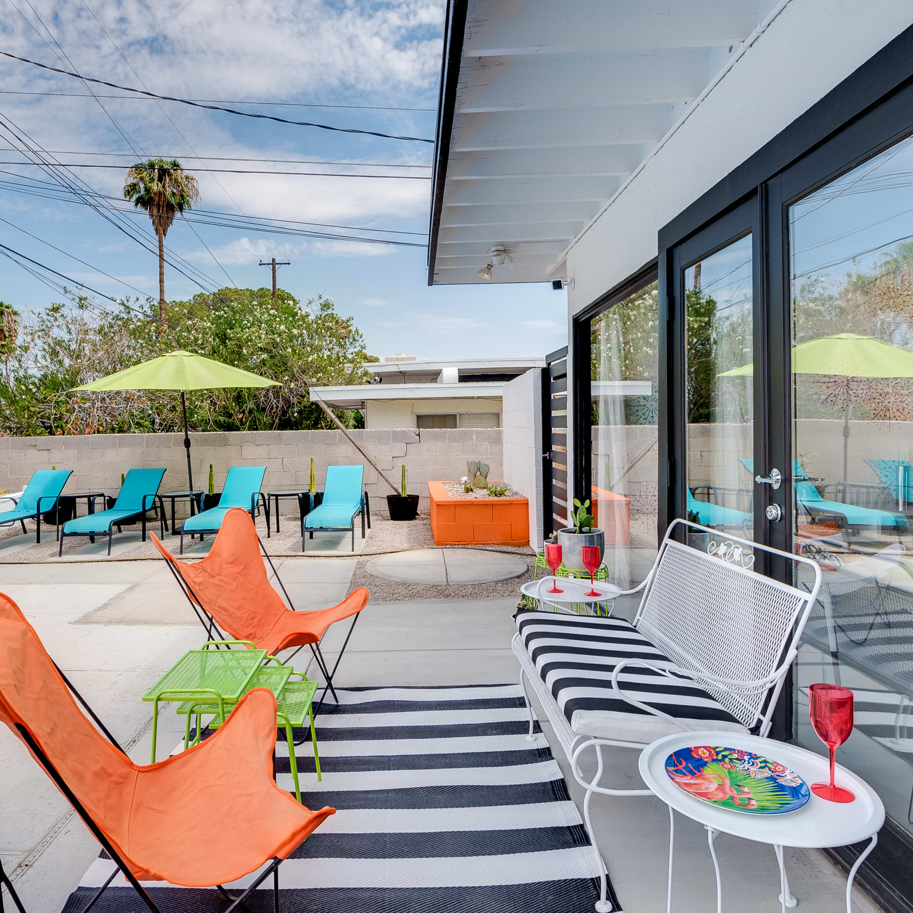 A patio area with a swimming pool, featuring orange chairs, a green table, and several lounge chairs under umbrellas.