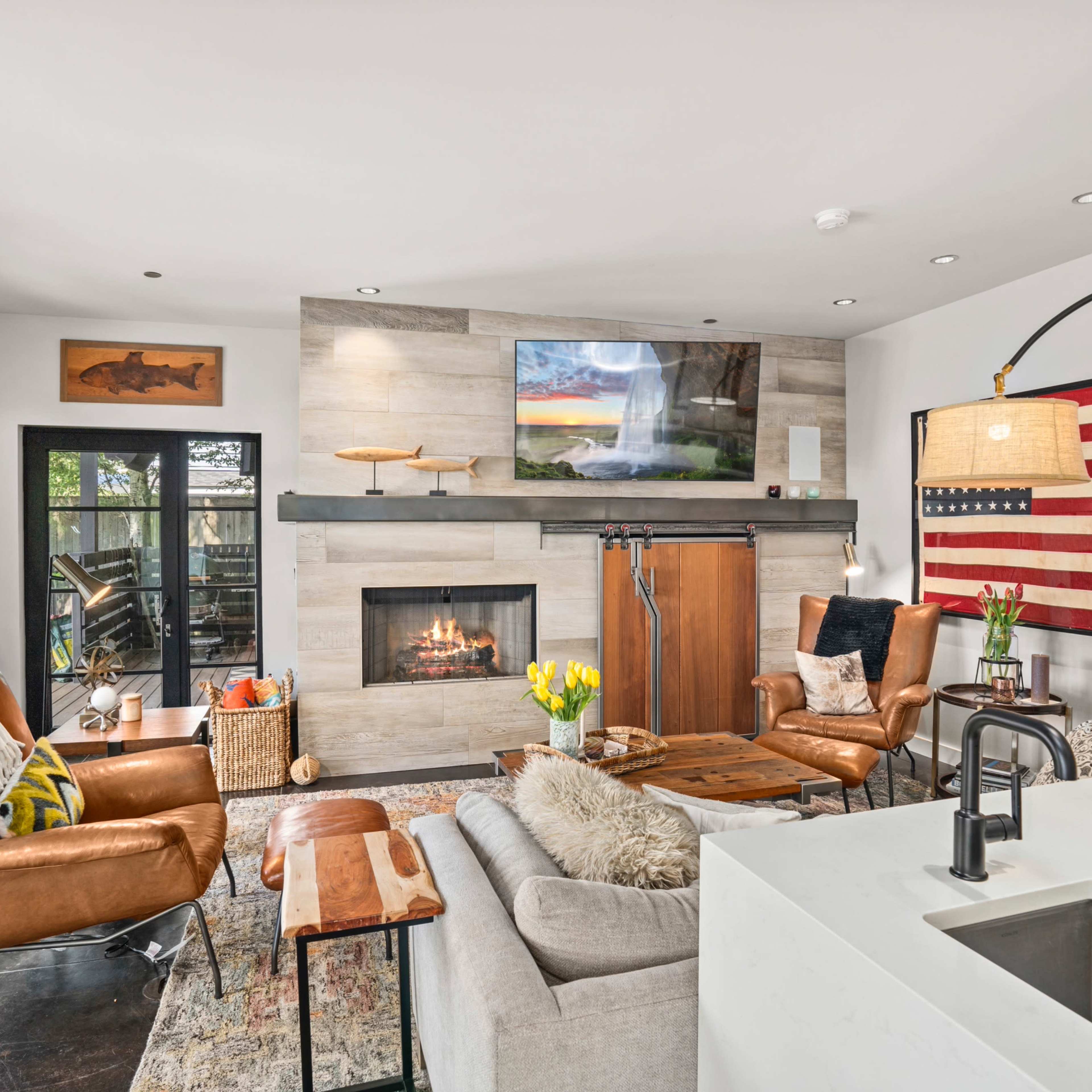 The living room features a modern design with a fireplace, wall-mounted television, leather seating, and large windows.