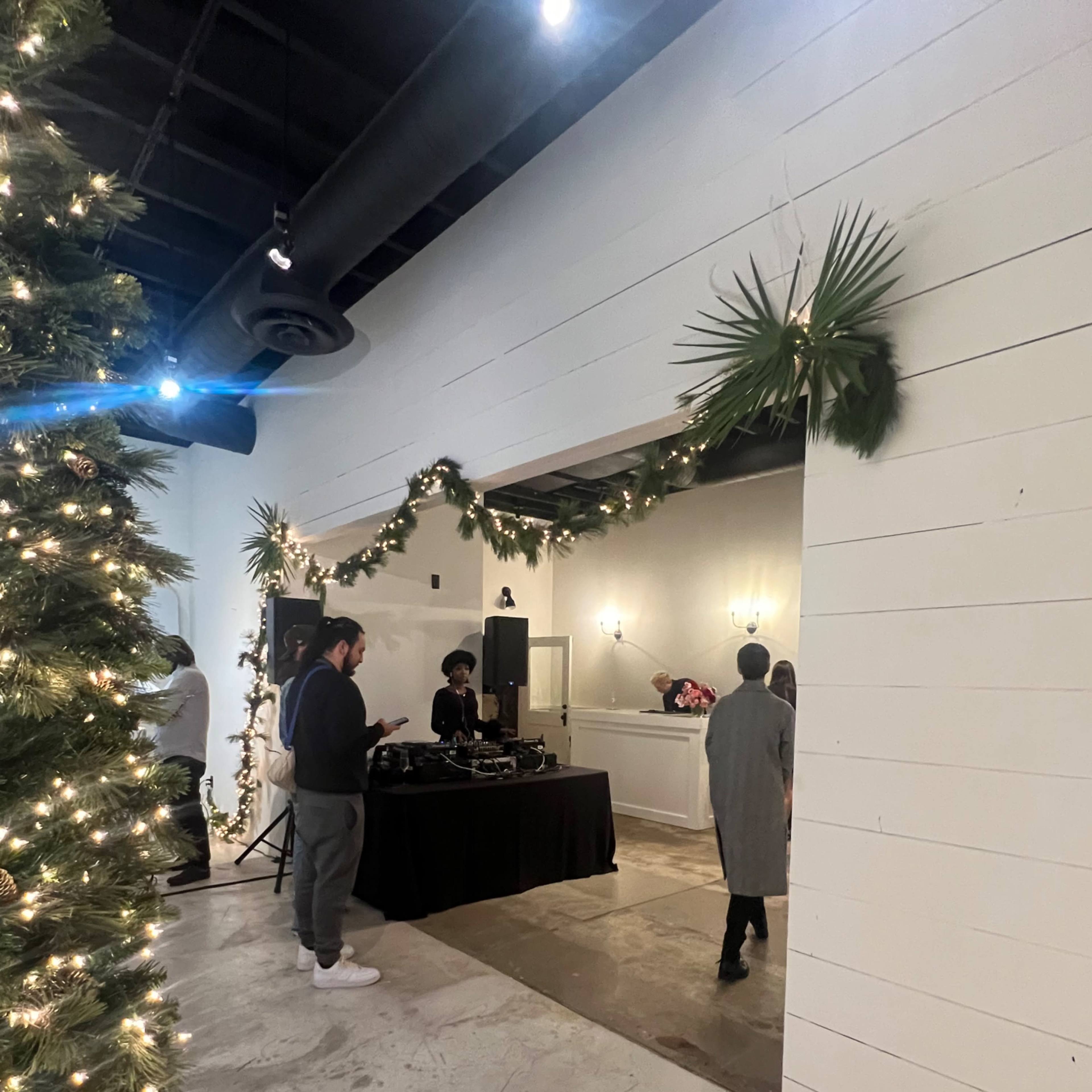 A party scene with a DJ setup and guests mingling under festive decorations, including string lights and greenery.