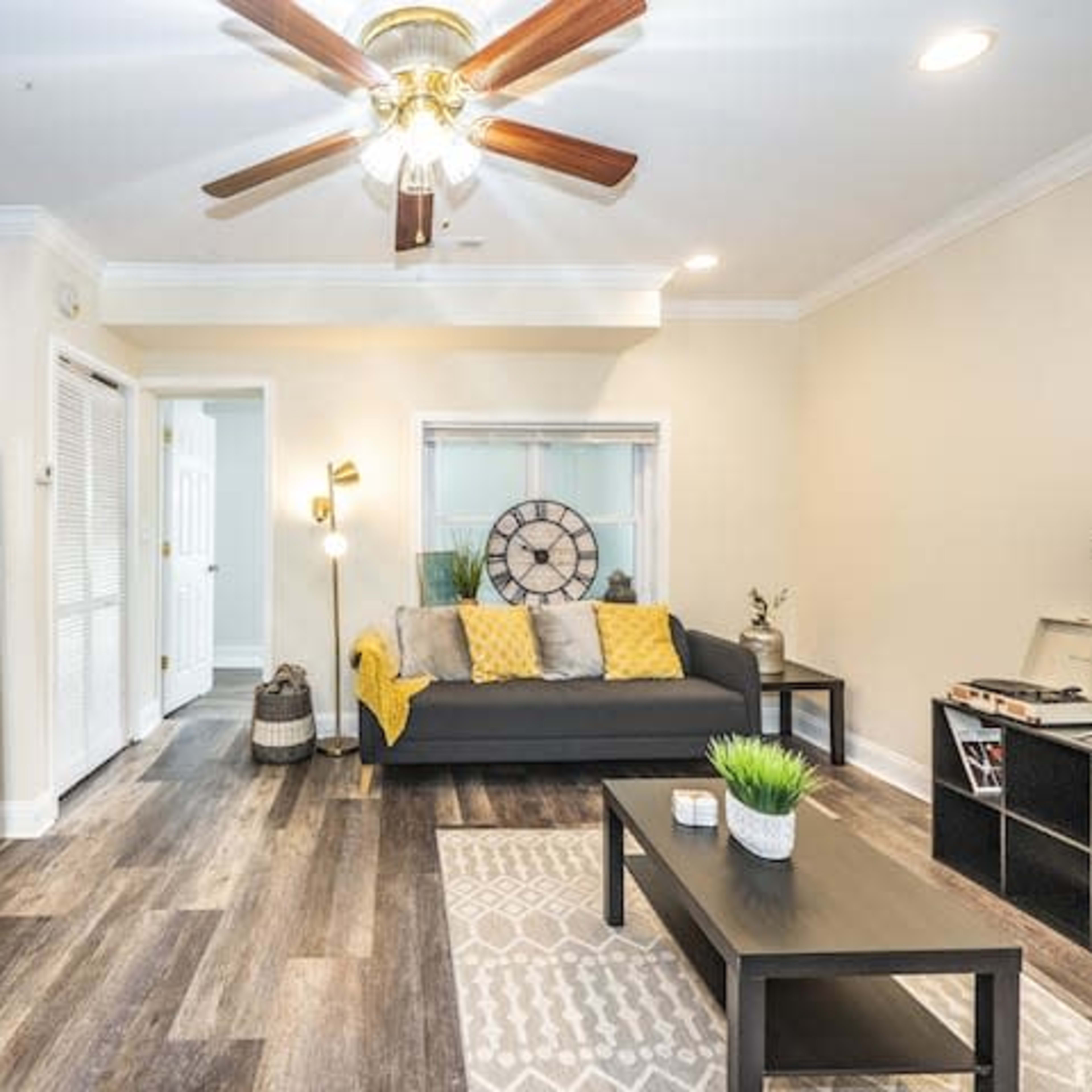 A living space with a couch, a coffee table, a television, and a kitchen area featuring a stainless steel refrigerator and wooden cabinets.