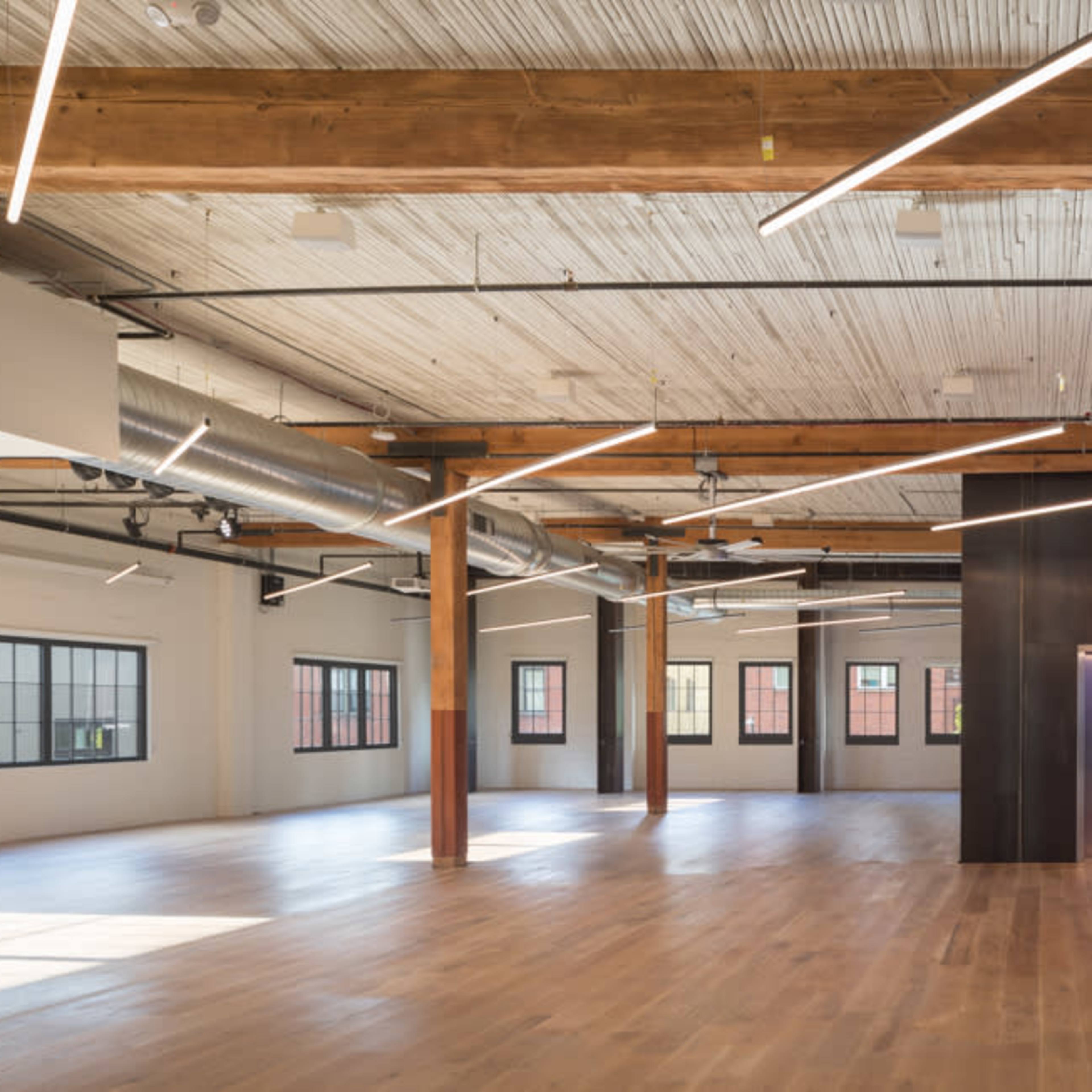 A spacious interior with wooden beams, large windows, and modern lighting, featuring an elevator and polished wooden floors.