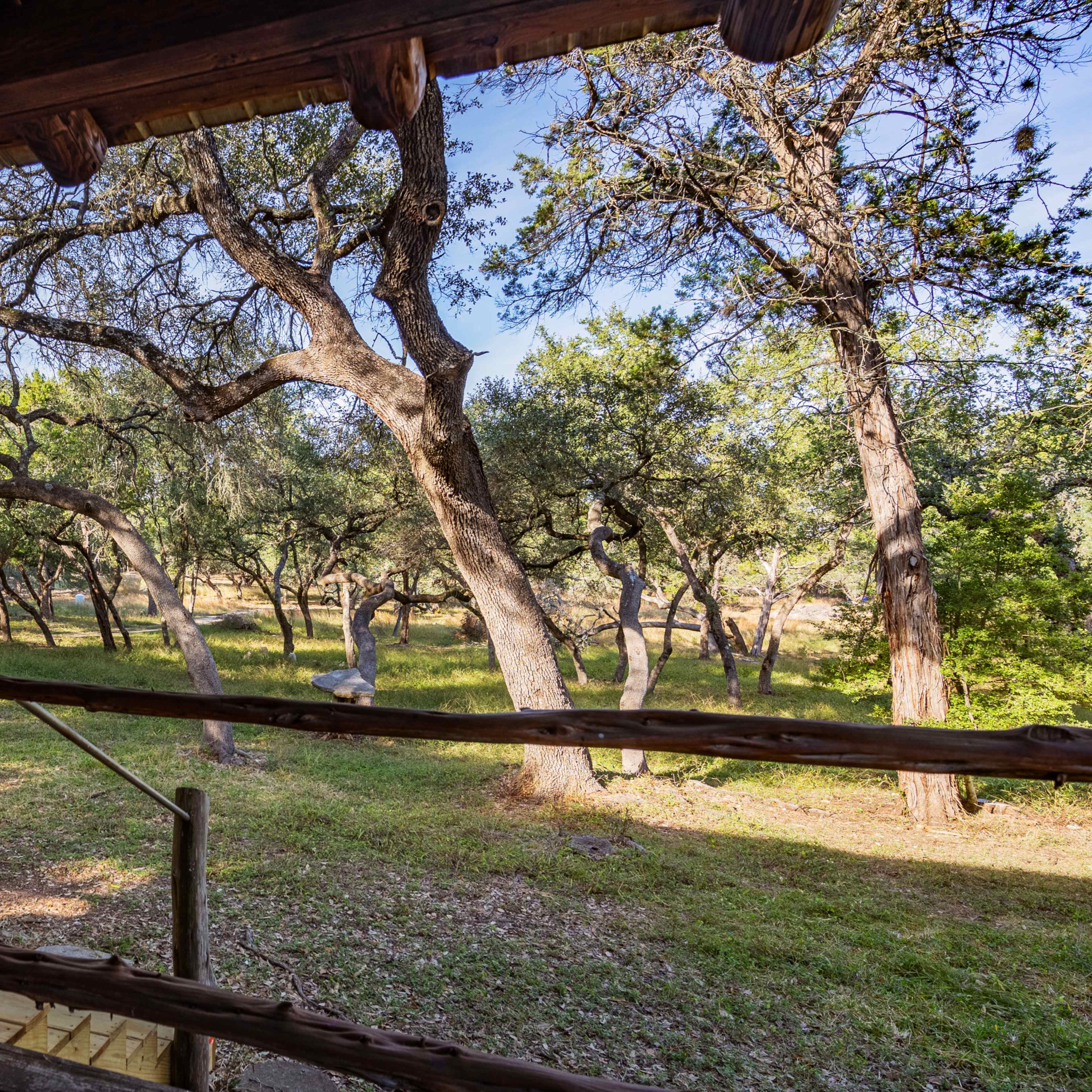 A wooden balcony overlooking a grassy area with several scattered trees.
