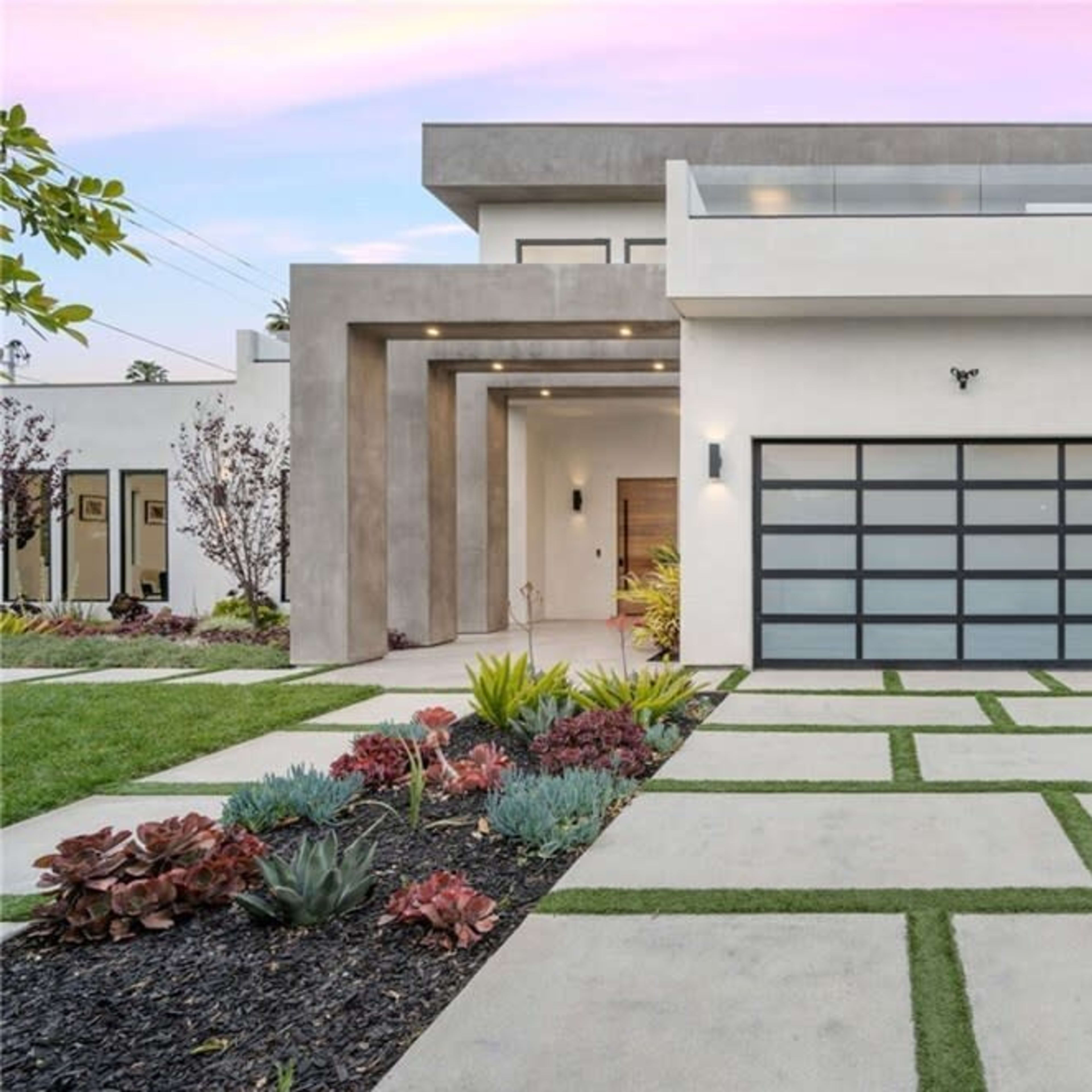 A modern house with a sleek exterior, featuring a large front yard and a driveway made of concrete with grass in between the slabs.
