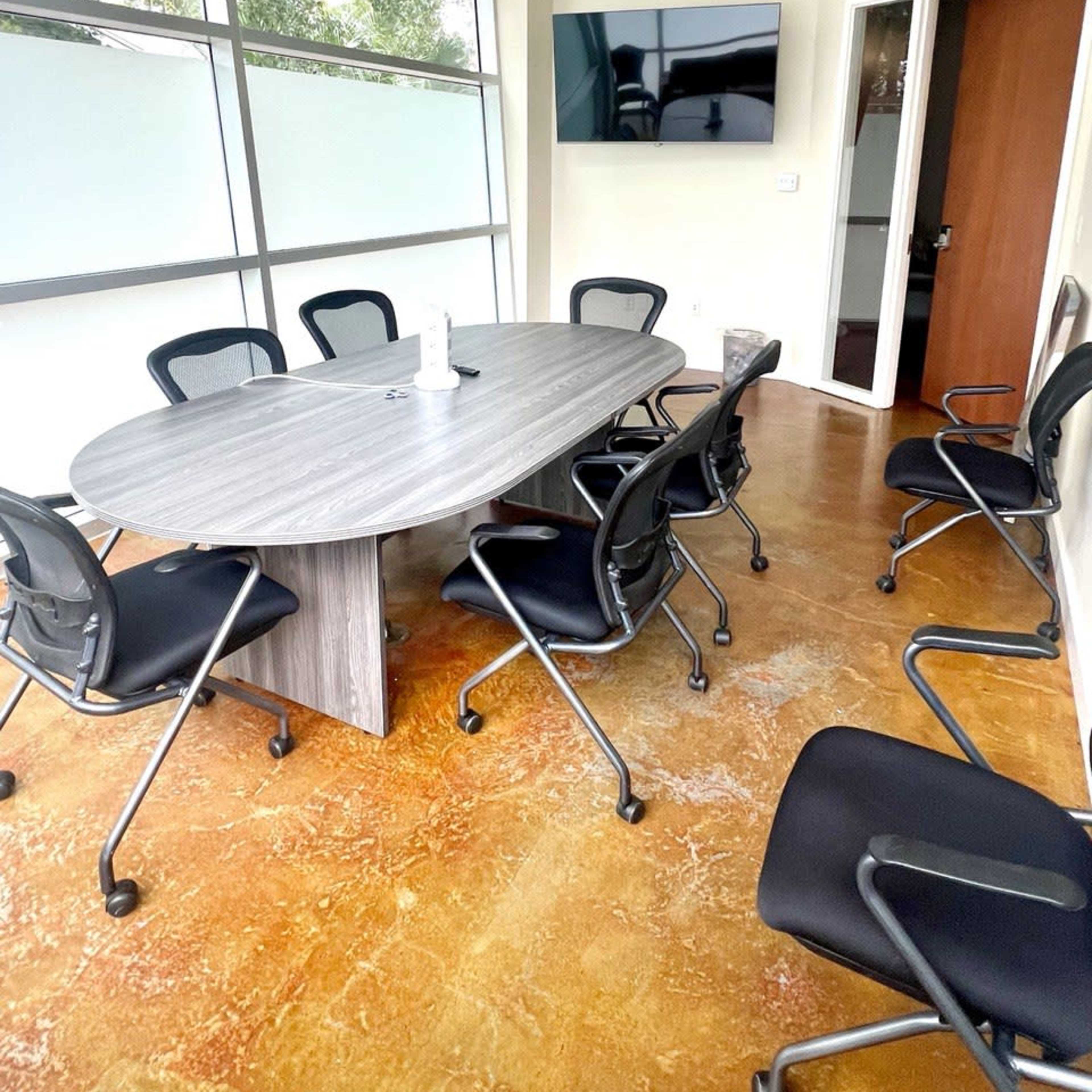 A conference room with a large oval table surrounded by black rolling chairs and a wall-mounted television.