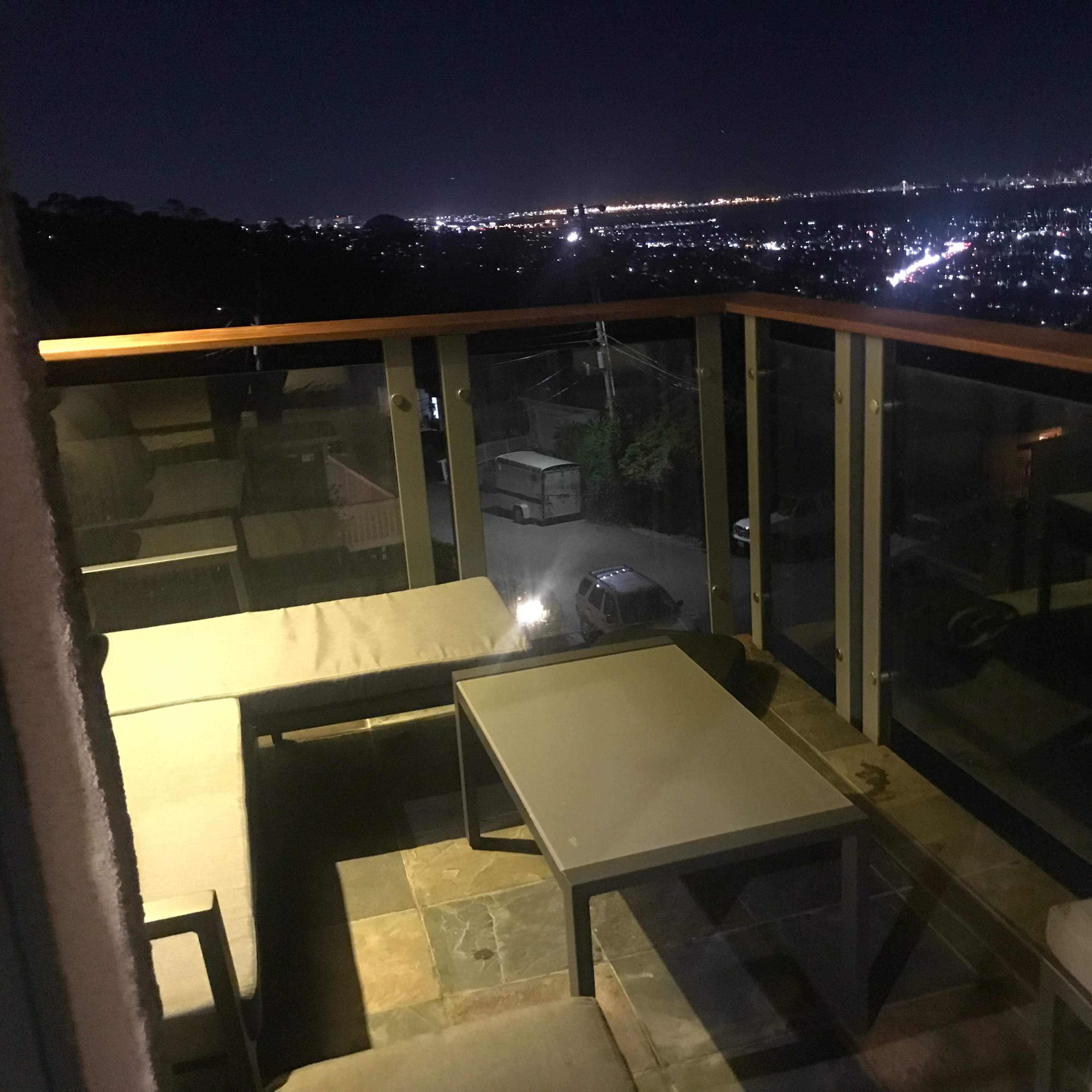 A balcony at night with modern furniture overlooking a cityscape illuminated by lights.