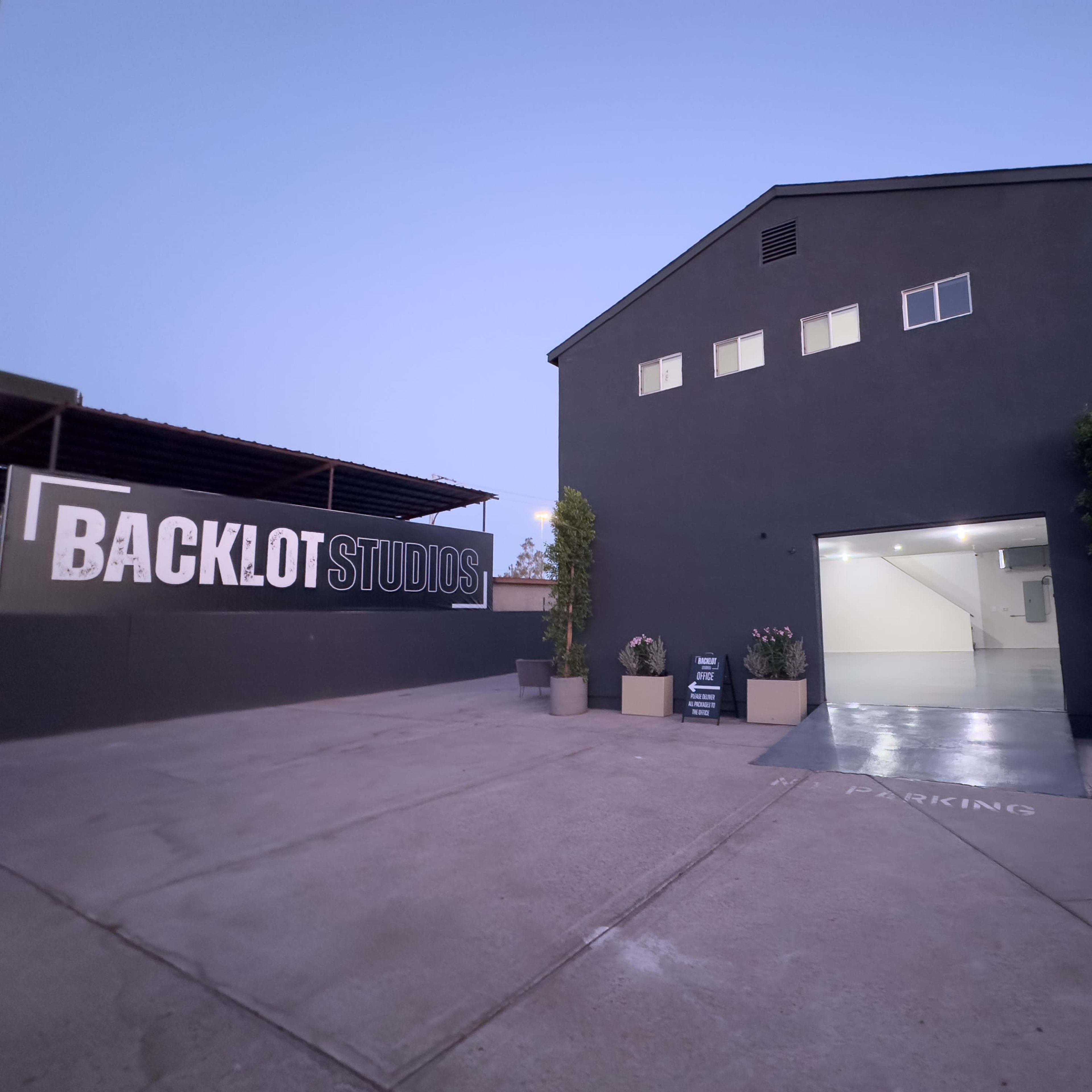 The exterior of Backlot Studios, featuring a dark building with a large open garage door and landscaped planters at the entrance.